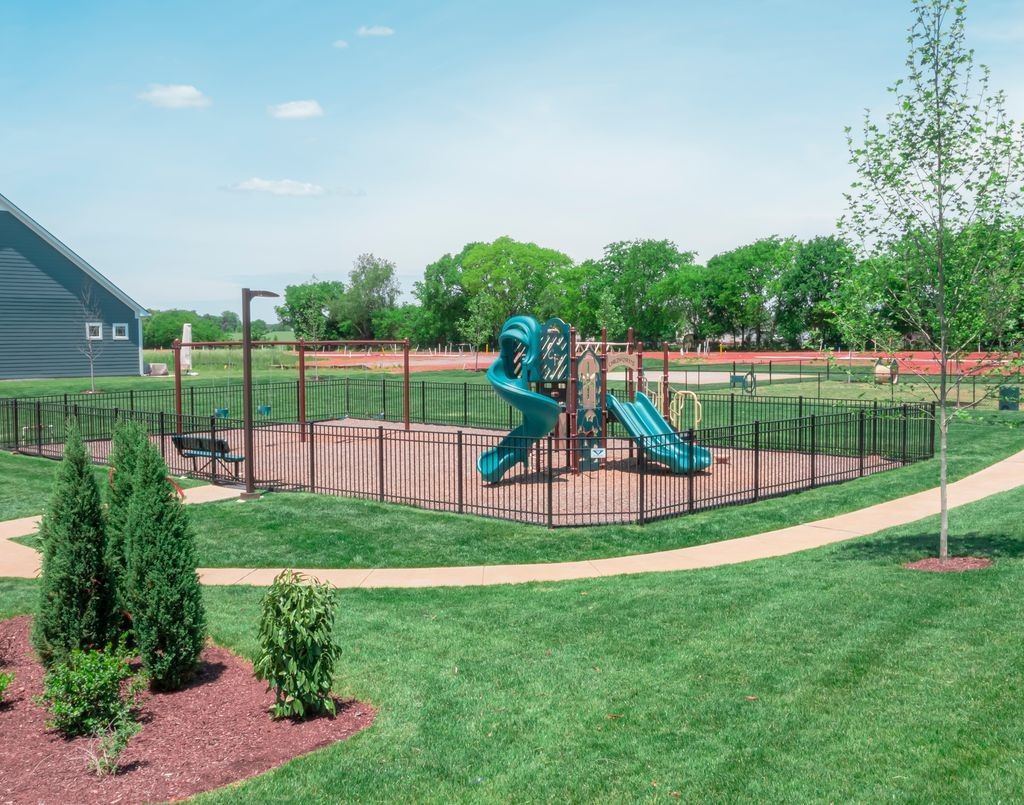 Children's playground with blue slides and swings in fenced grassy area, trees and path in Shelton Square, Murfreesboro, Tennessee