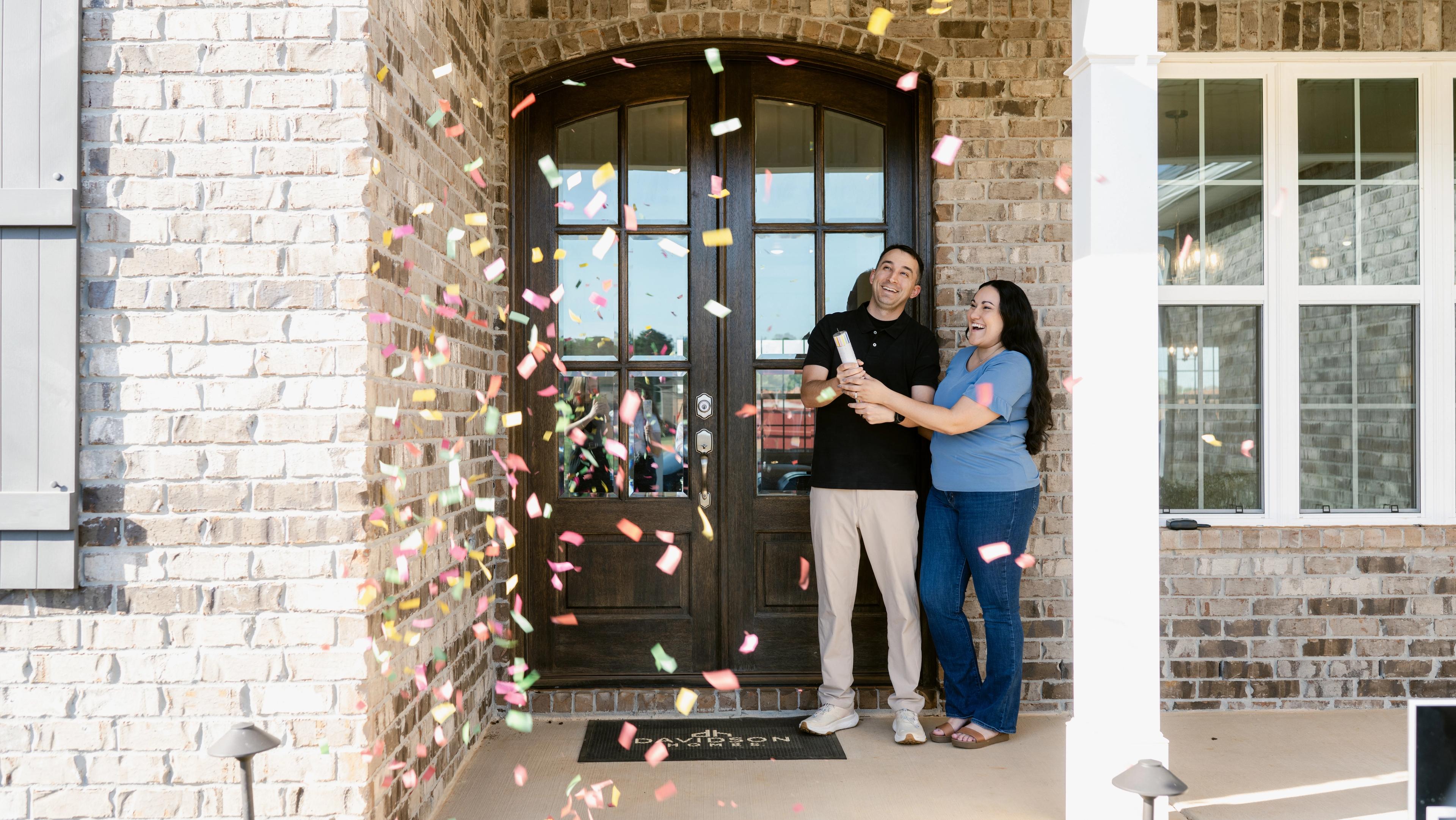 Joyful couple celebrating with colorful confetti outside new brick Davidson Homes in Houston TX
