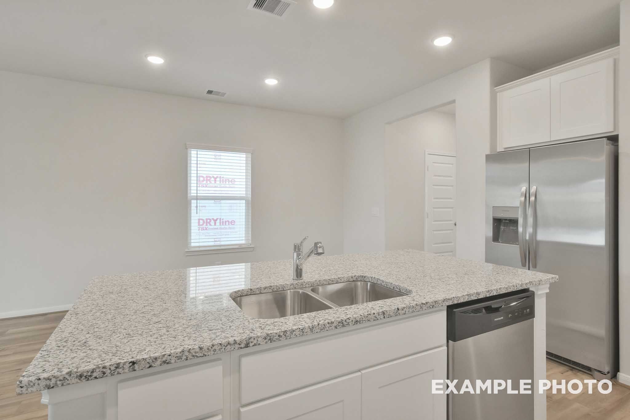 Kitchen island with granite countertops and double sink in The Brazos by Davidson Homes, Beasley TX