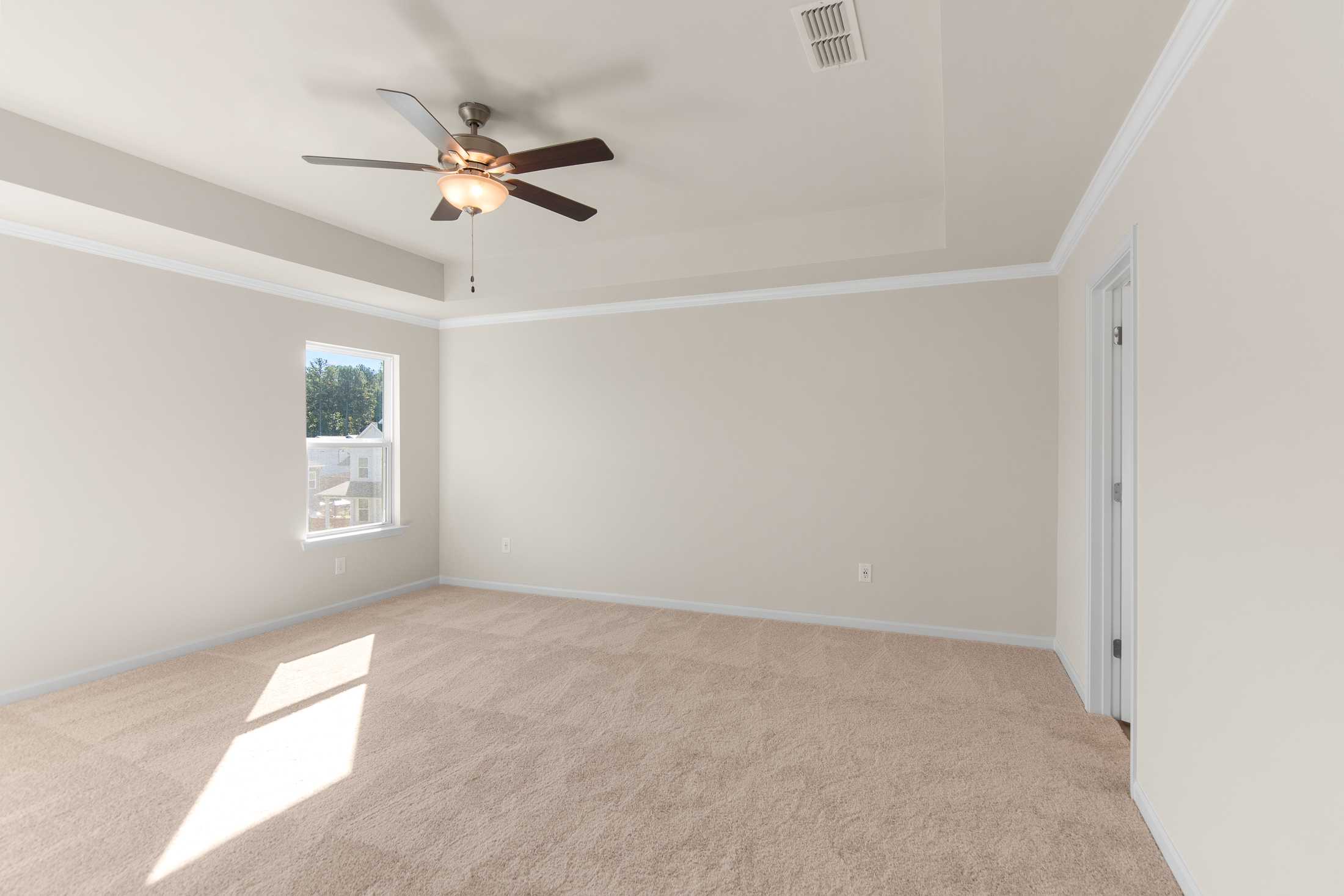 Spacious master bedroom in The Willow B featuring ceiling fan, large window with blinds, beige walls, and carpeted floor