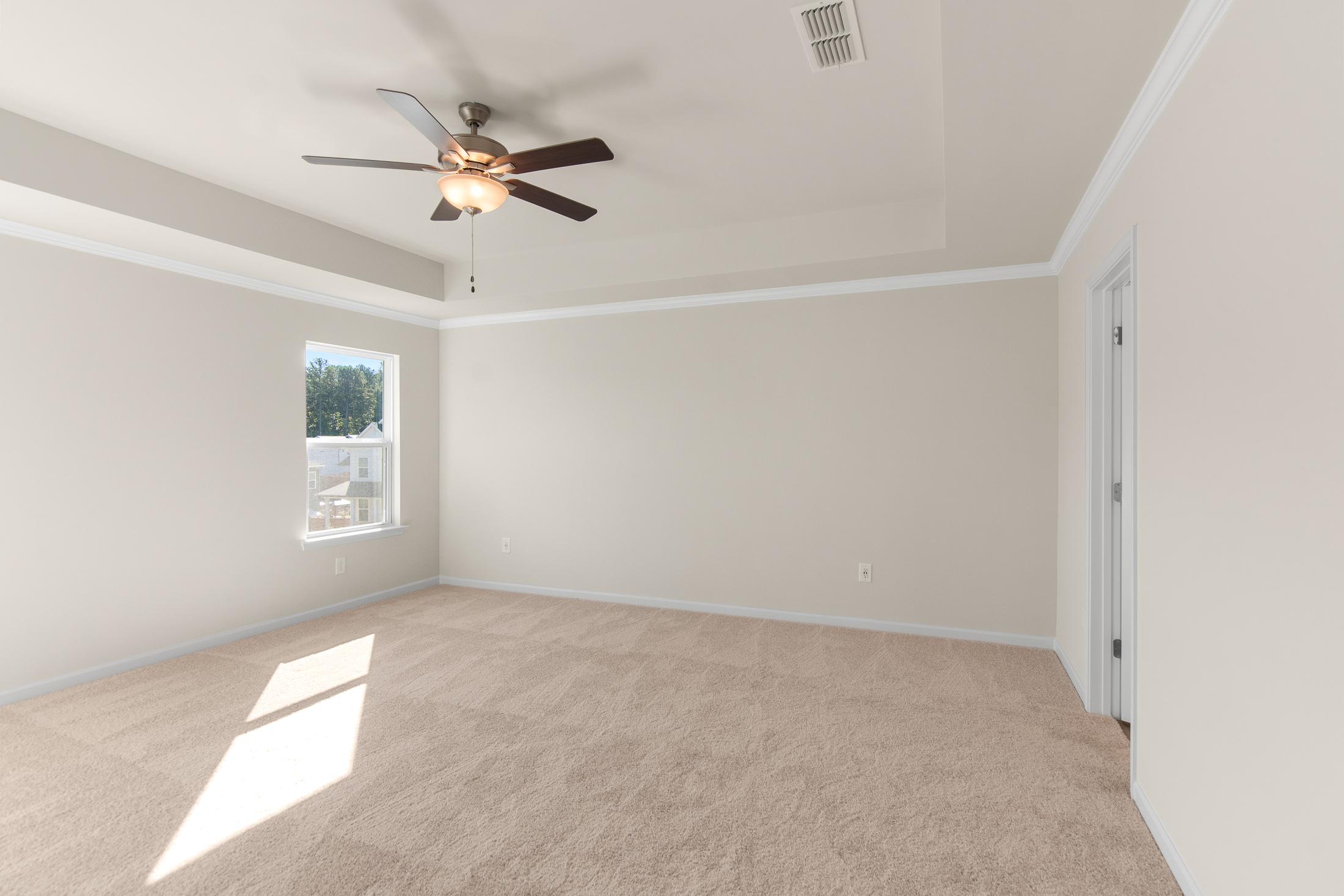 Spacious master bedroom in The Willow B featuring ceiling fan, large window with blinds, beige walls, and carpeted floor