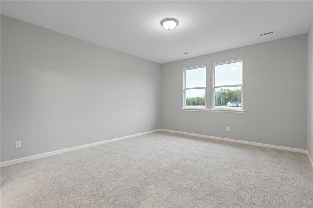 Bright empty bedroom with light gray walls, beige carpet, and double windows in Davidson Homes The Luna B, Opelika, AL