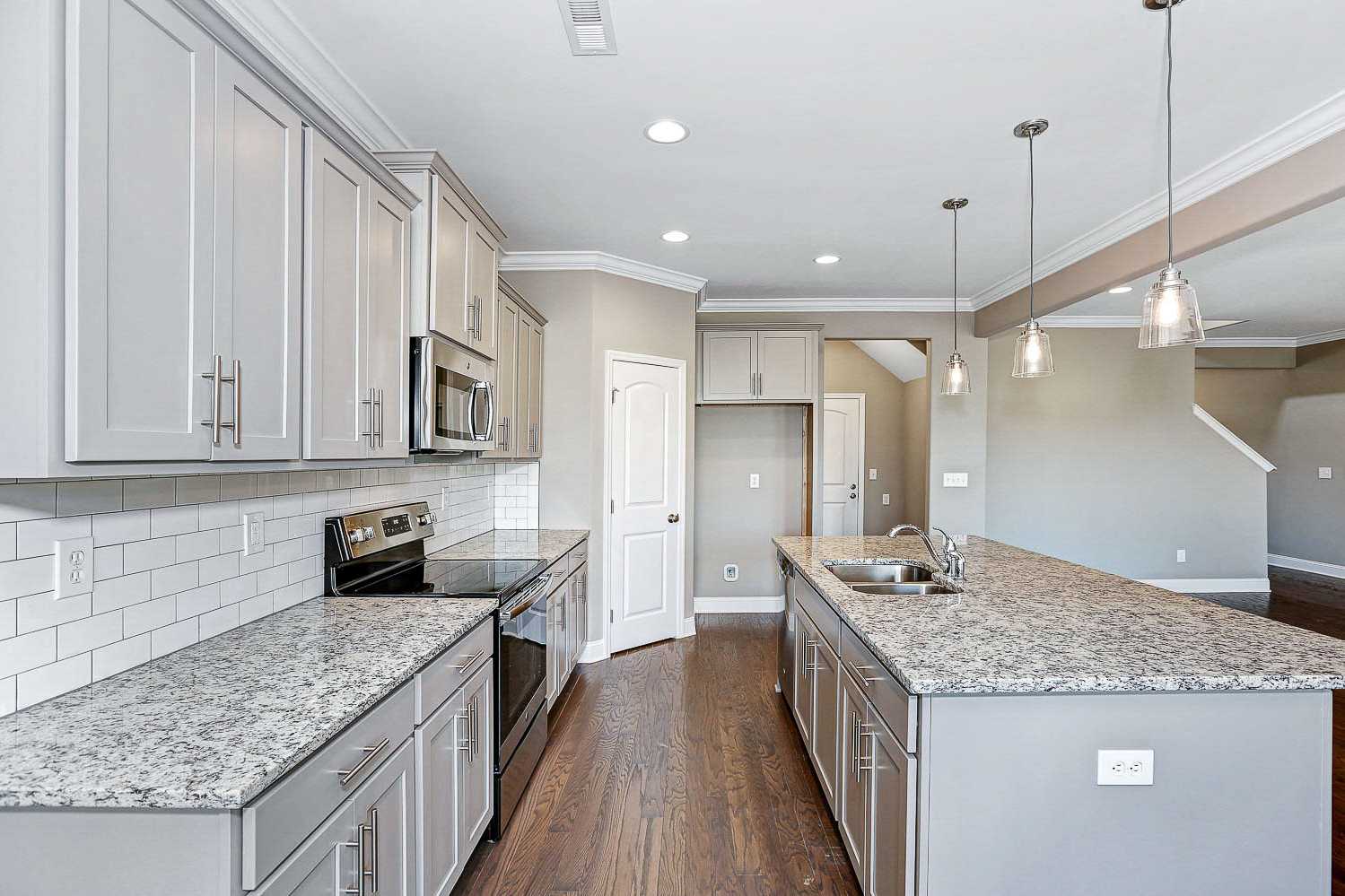 Spacious kitchen in The Montgomery with white shaker cabinets, granite island, subway tile backsplash, and stainless appliances
