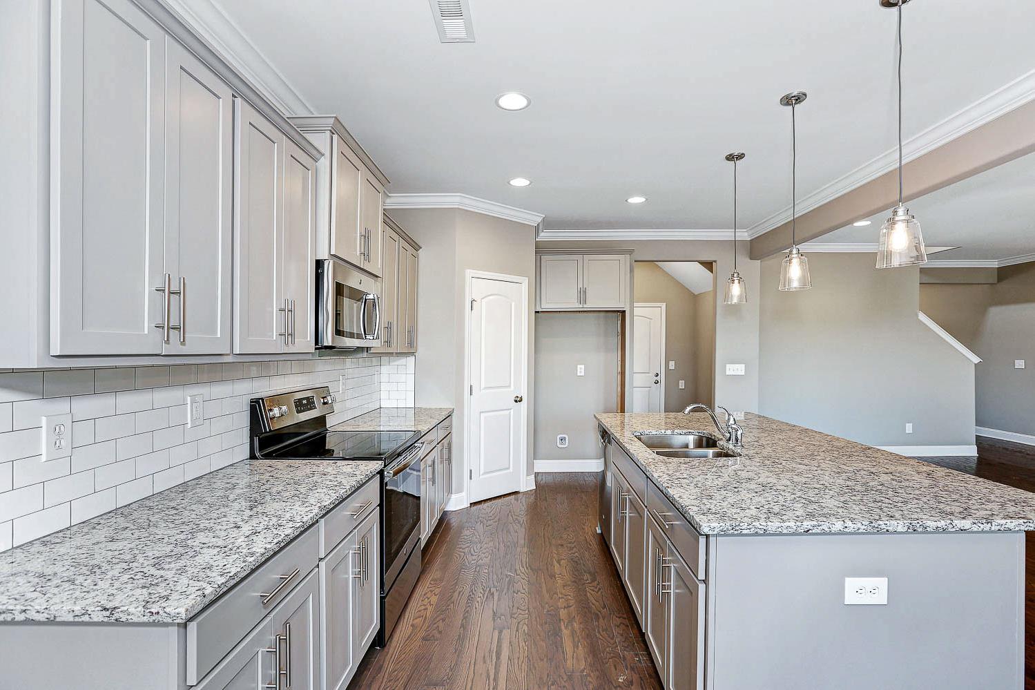 Spacious kitchen in The Montgomery with white shaker cabinets, granite island, subway tile backsplash, and stainless appliances