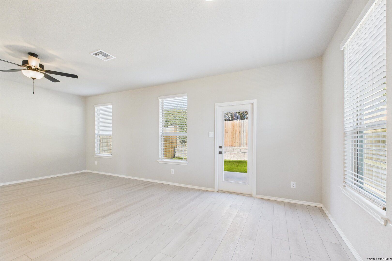 Bright living room with light wood floors, ceiling fan, and backyard view in Davidson Homes The Charlotte A, San Antonio