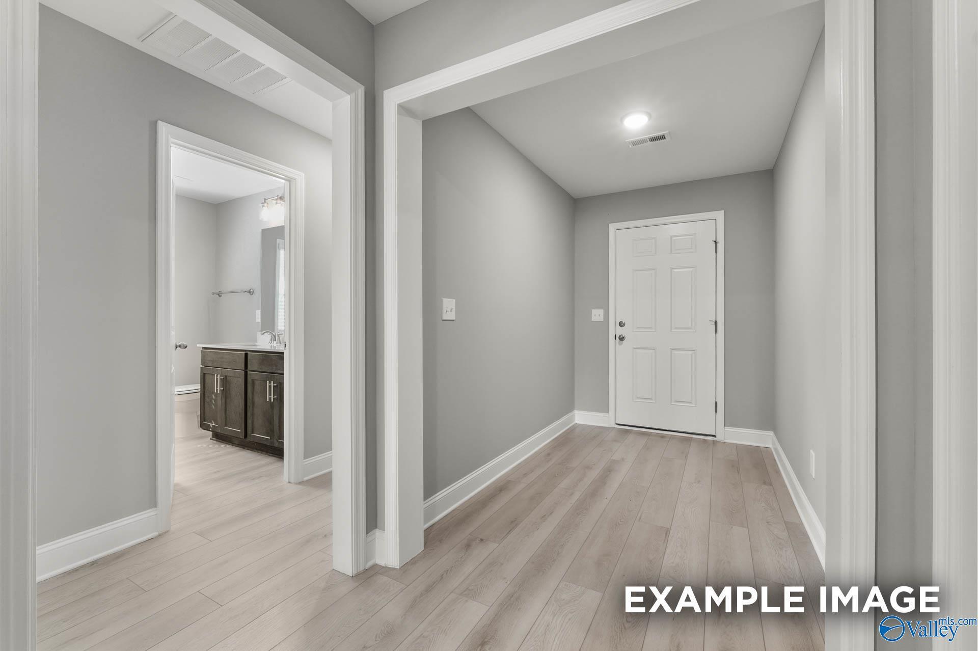 Modern hallway with gray walls, light wood floors, open bathroom vanity, and white bedroom door in The Everett B, Toney, Alabama