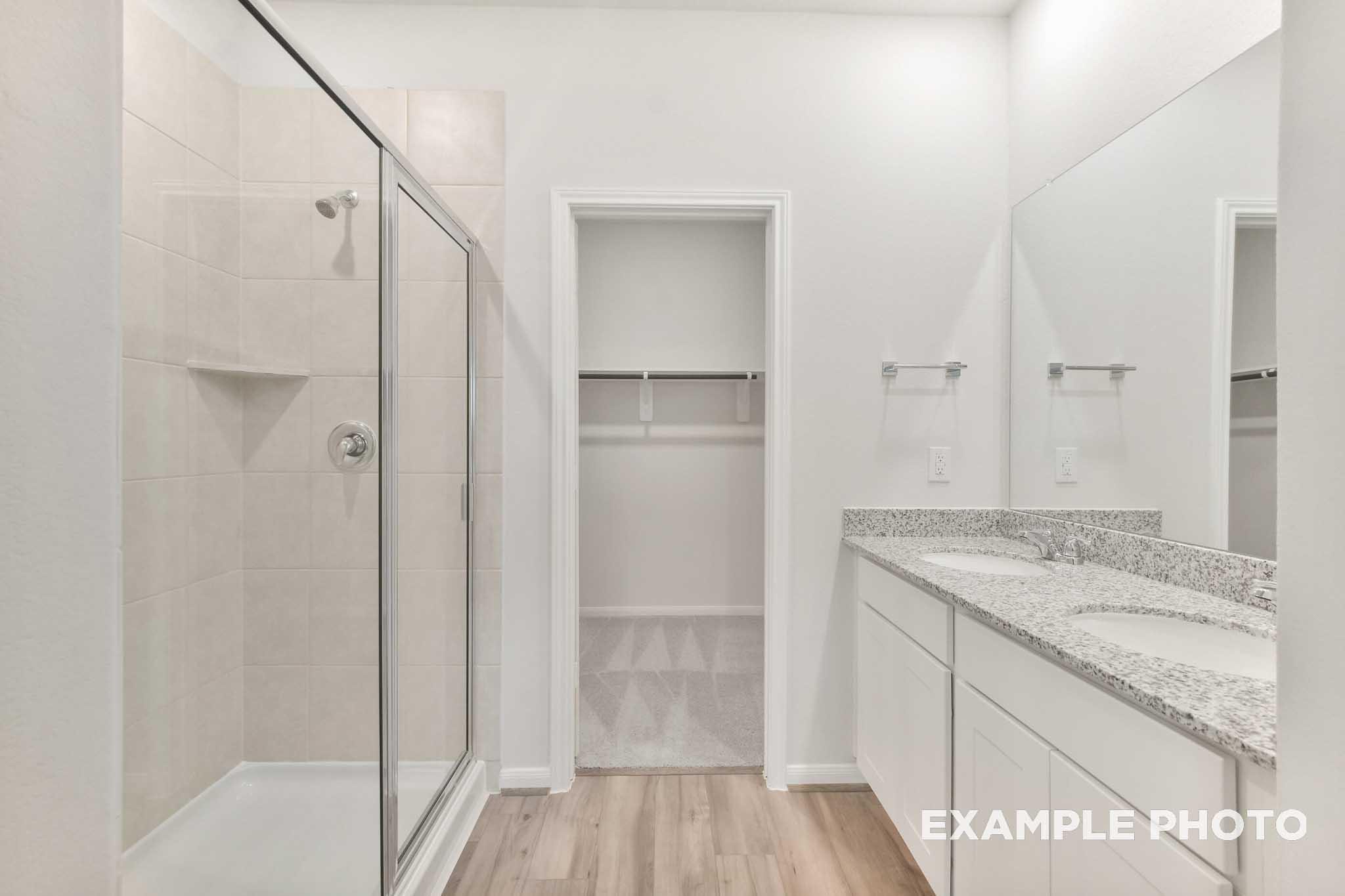 Master bathroom in The Brazos by Davidson Homes featuring glass shower, double vanity with granite countertops, and walk-in closet