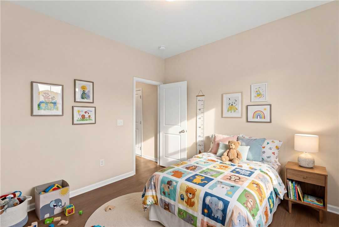 Cozy children's bedroom with twin bed, colorful animal quilt, teddy bear, toys, and wall art in Evermore Homes The Orion, Cusseta, Alabama