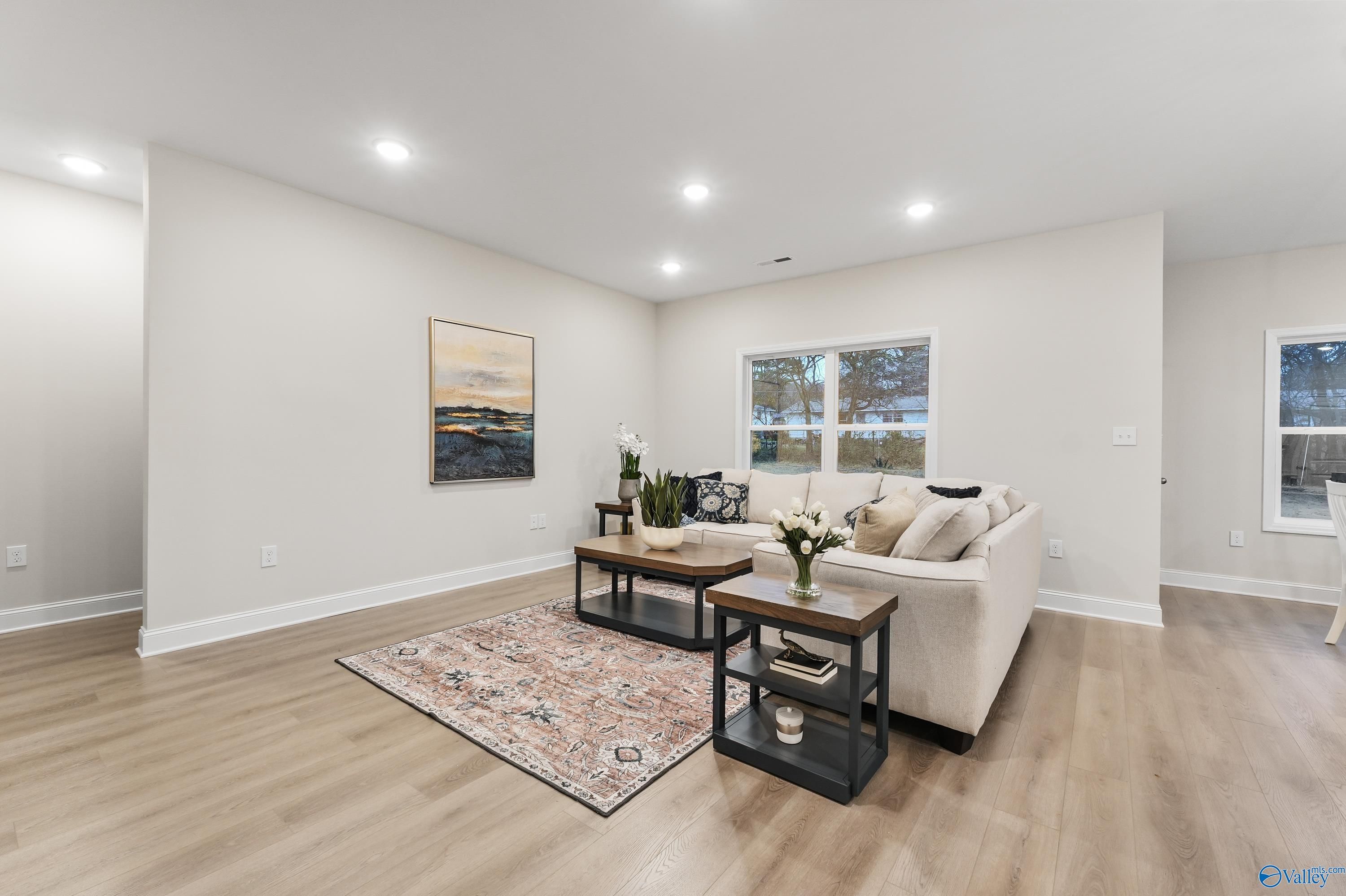 Cozy living room with beige sofa, wooden coffee table, potted plants, and large windows in Davidson Homes The Asheville C, Huntsville AL