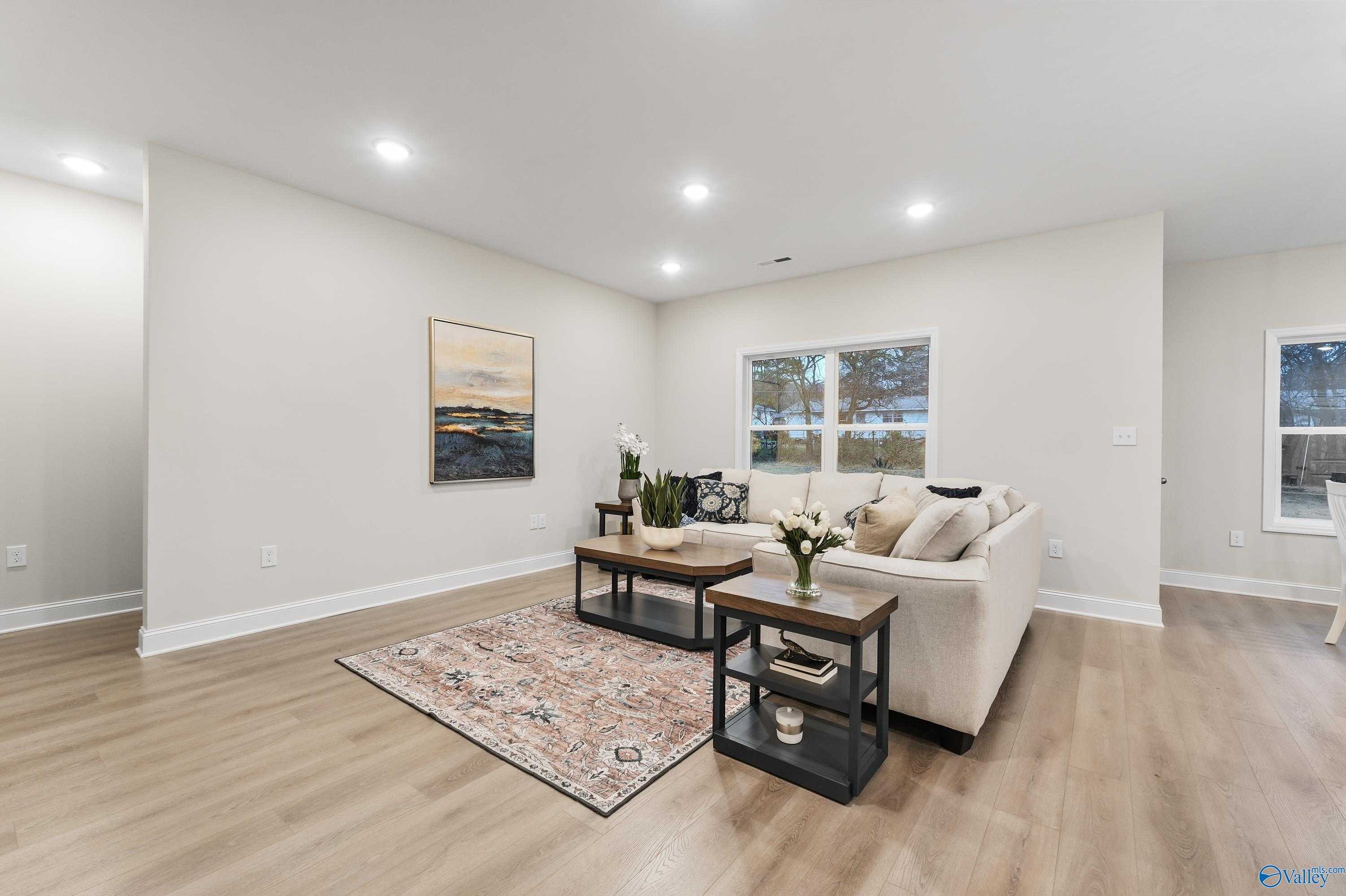 Cozy living room with beige sofa, wooden coffee table, potted plants, and large windows in Davidson Homes The Asheville C, Huntsville AL