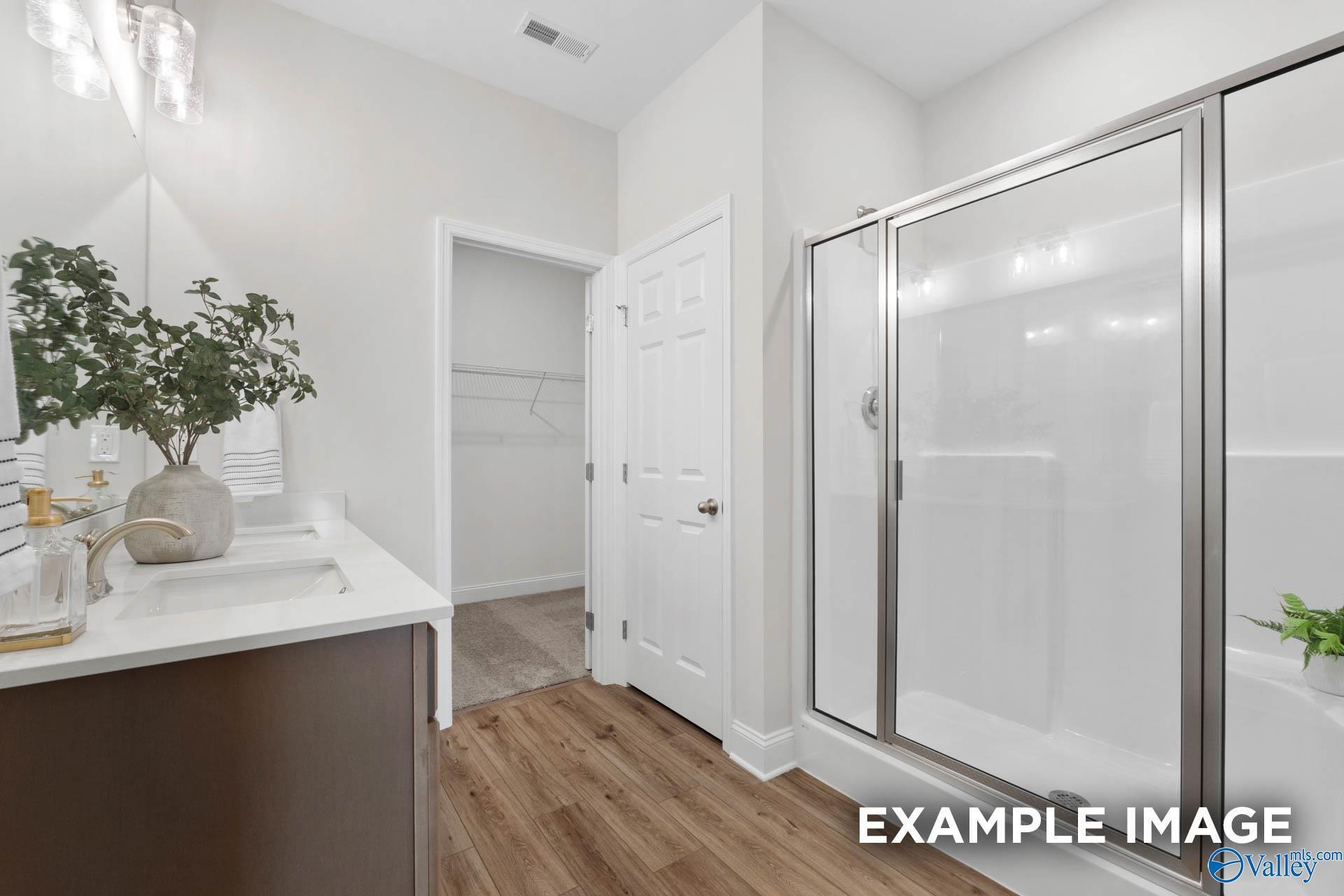 Modern bathroom with dual vanity, glass-enclosed shower, and walk-in closet in The Franklin C plan, Heritage Lakes.