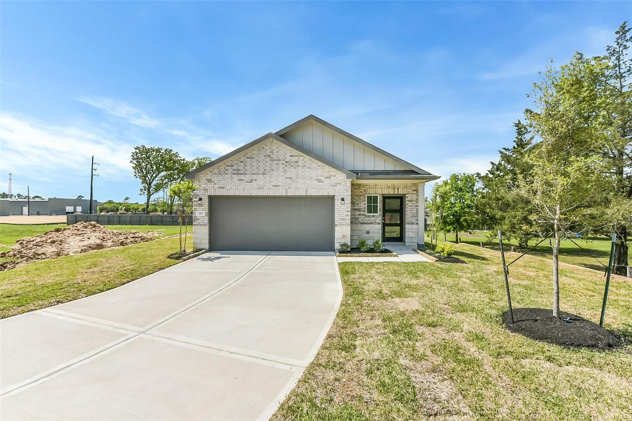 White brick single-story 3-bedroom home with 2-car garage, driveway, and trees in Windmill Estates, Magnolia, Texas - Davidson Homes The Frio G