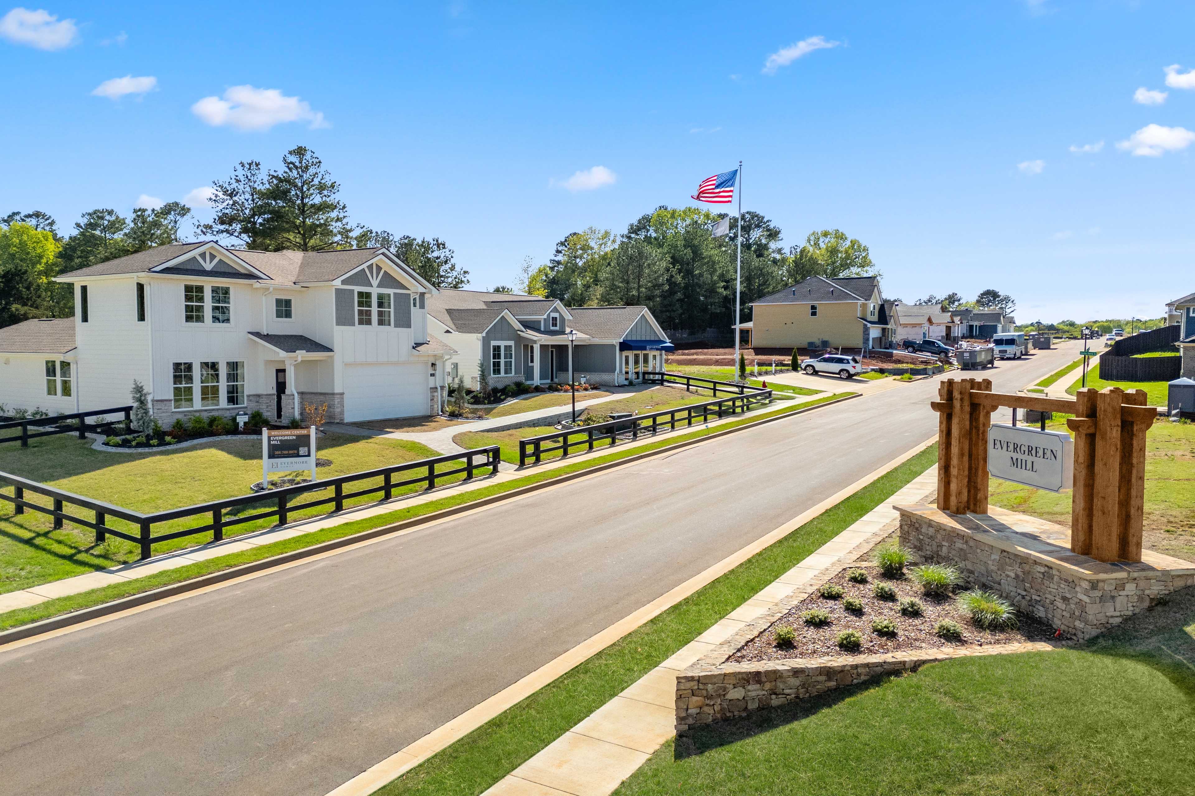Evergreen Mill neighborhood entrance in Madison Alabama featuring modern homes, American flag, welcome sign, black fences, and lush landscaping