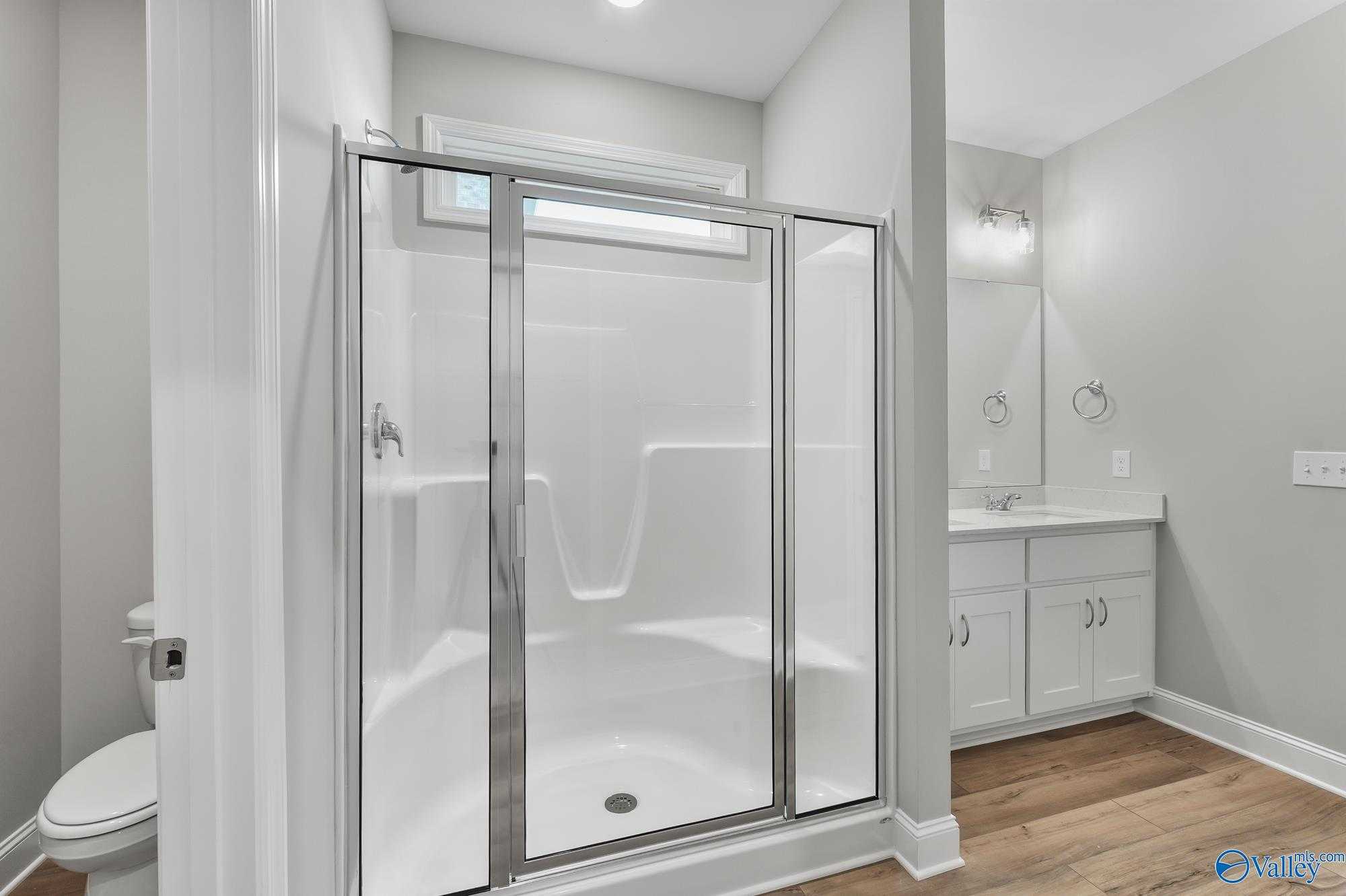 Modern bathroom with frameless glass shower, white tile surround, and shaker-style vanity in Davidson Homes The Daphne D, Athens, AL