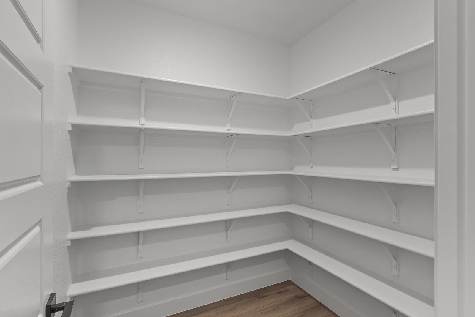 Spacious walk-in pantry with white wrap-around shelving in The Belmont J floor plan by Davidson Homes.
