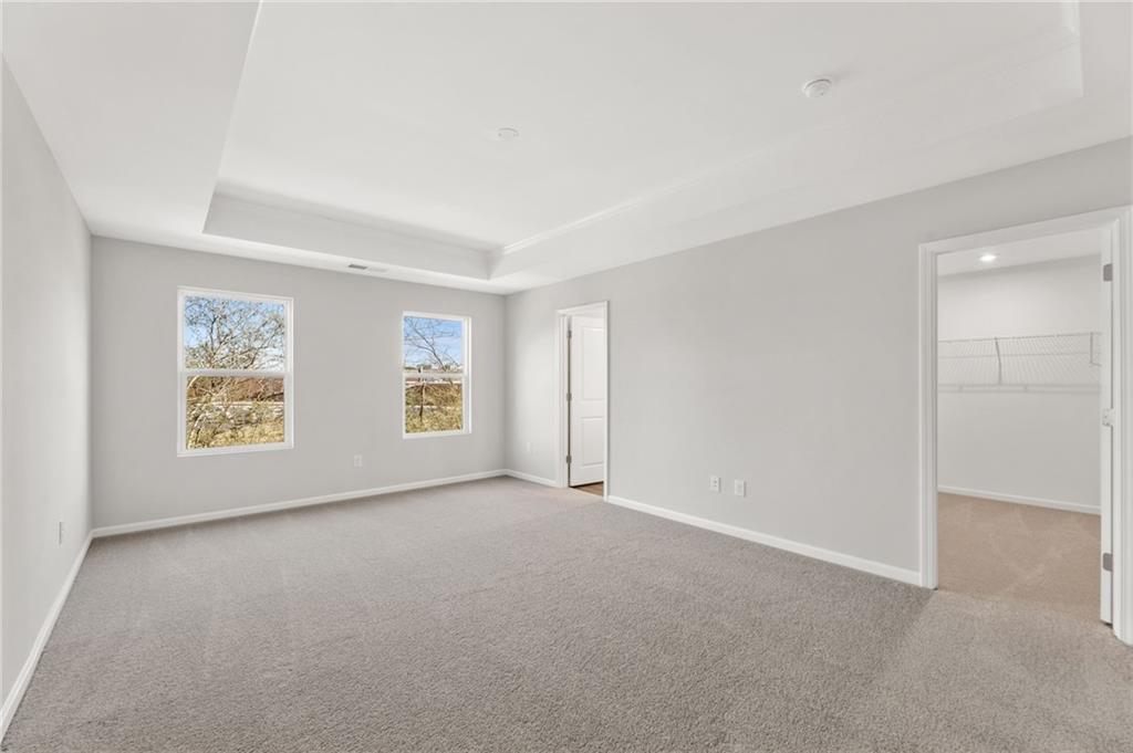 Bright secondary bedroom with large windows overlooking trees, gray walls, tray ceiling, and closet in Davidson Homes The Marion A, Winder, Georgia