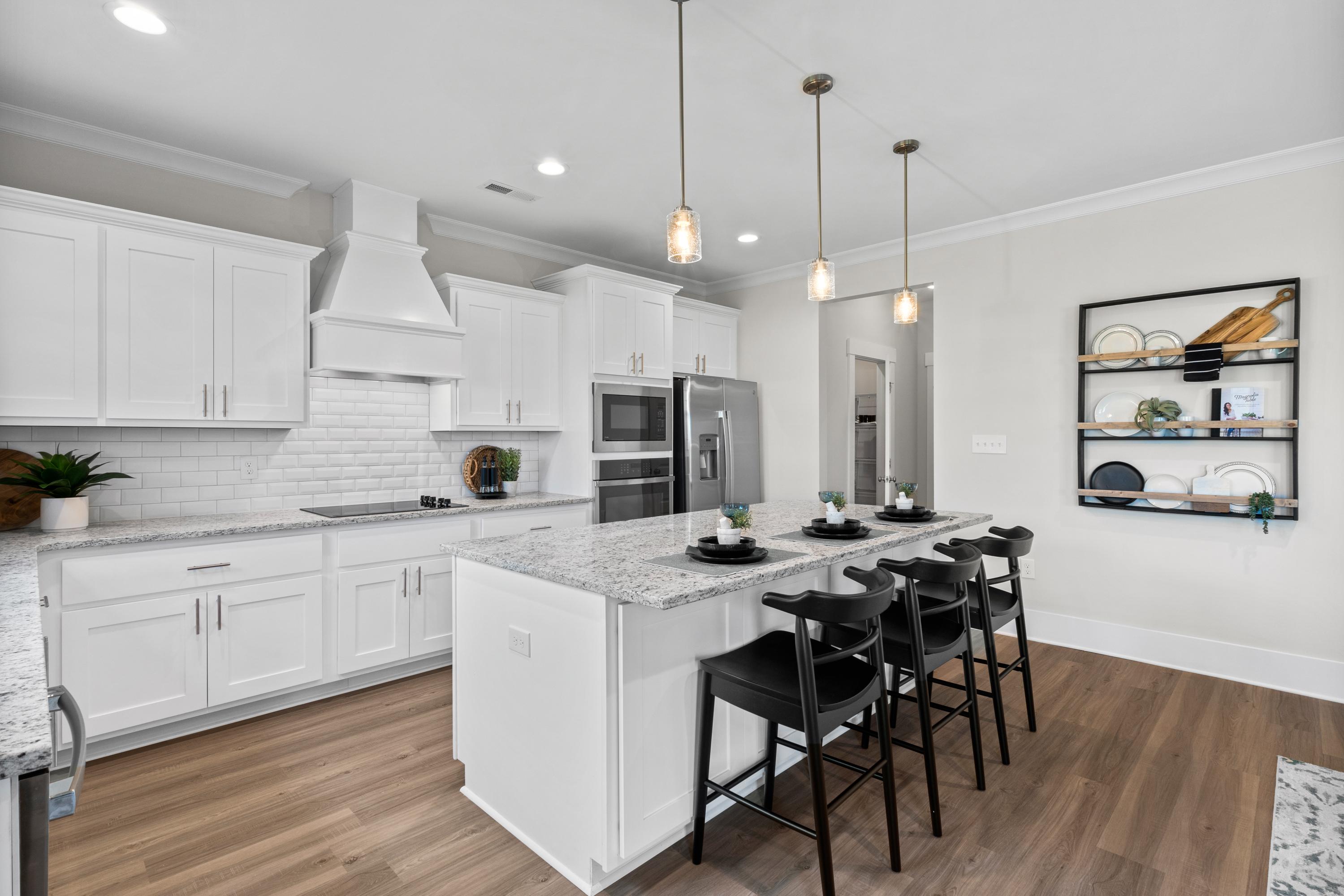 Spacious modern kitchen in The Chelsea A with white cabinets, large quartz island, black bar stools, subway tile backsplash, stainless appliances