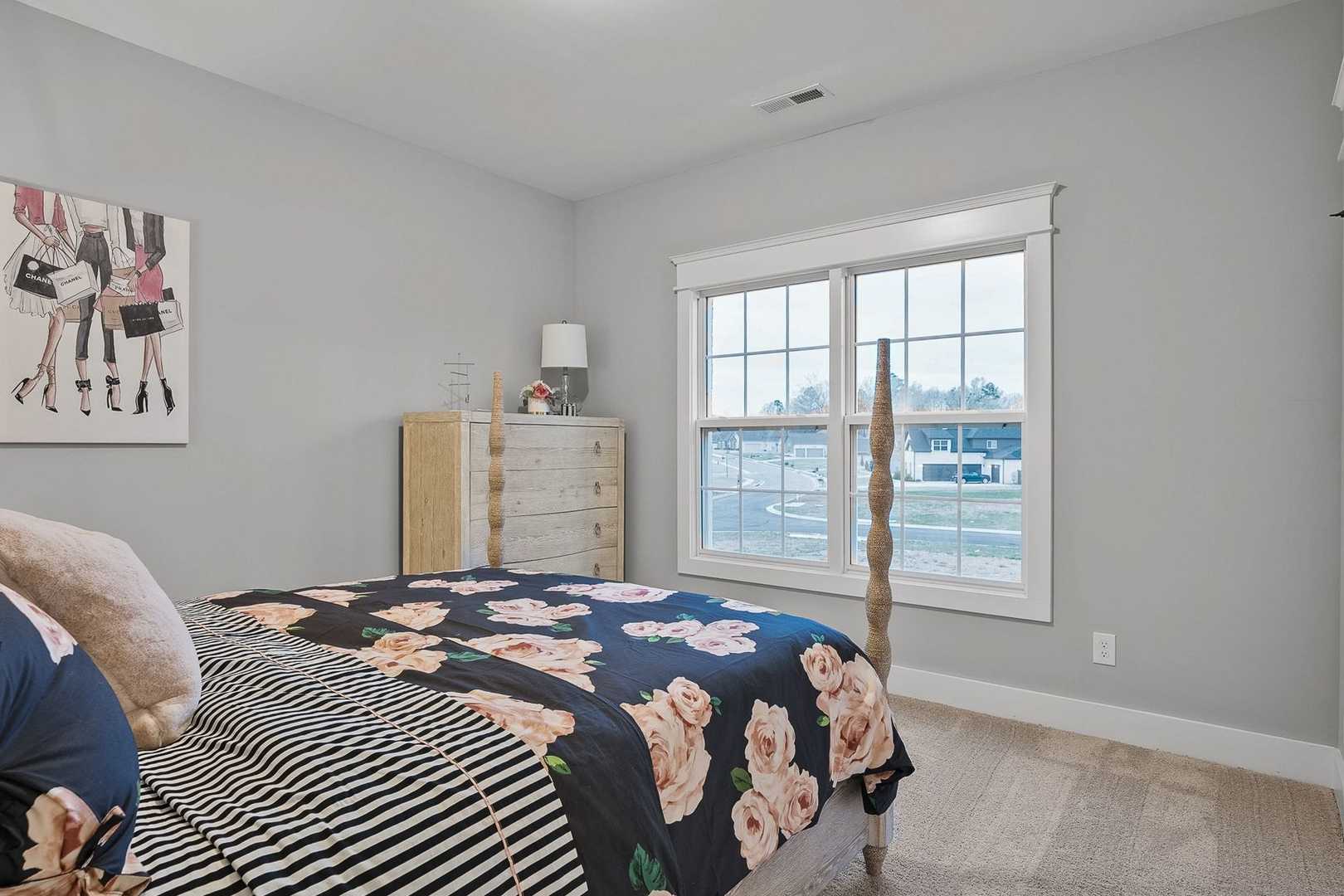 Spacious bedroom in The Oxford with floral bedding on king bed, gray walls, dresser, window view, and fashion artwork