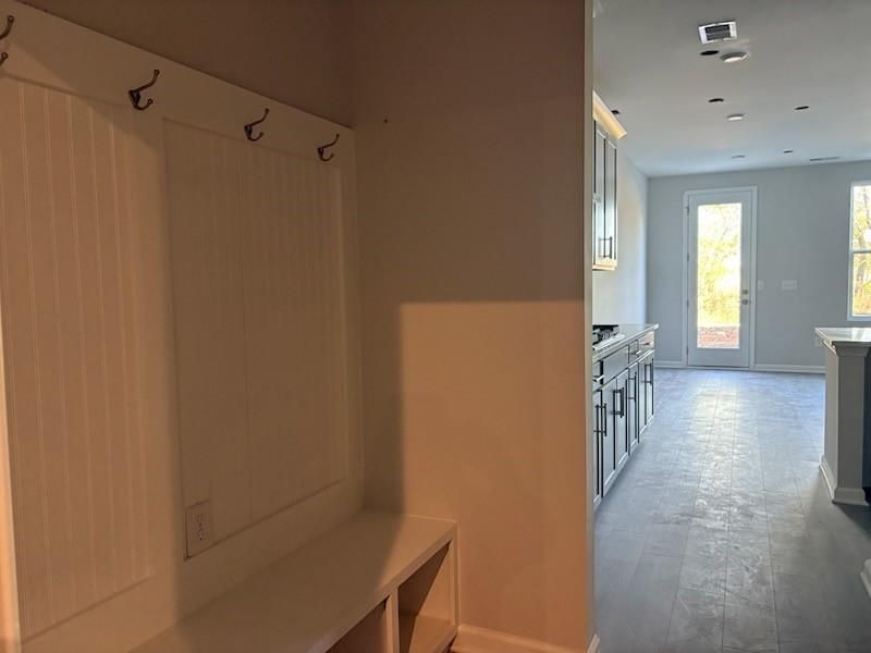 White coat hooks and bench in mudroom adjacent to modern kitchen with white cabinets in Davidson Homes Marion A, Winder Georgia