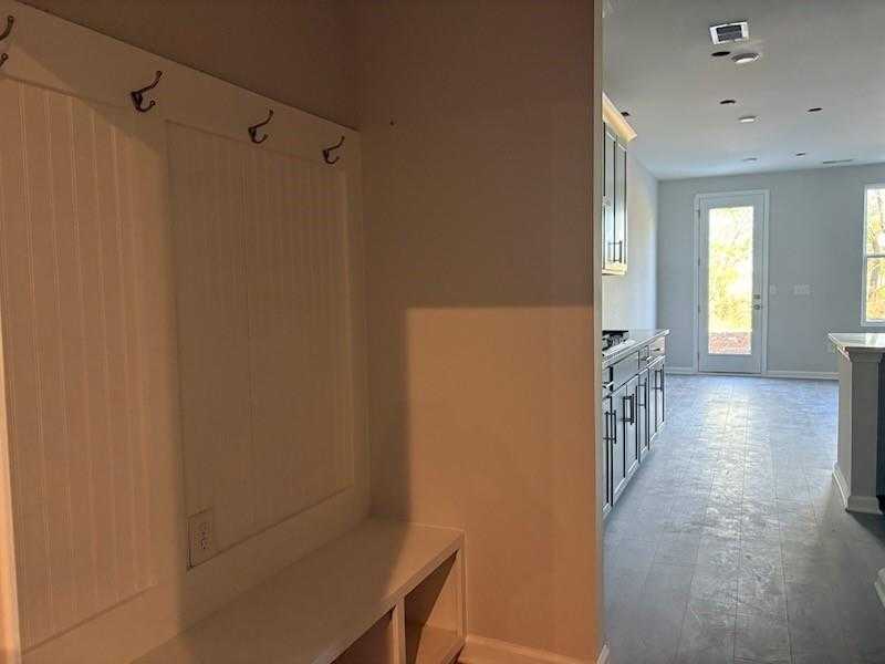 White coat hooks and bench in mudroom adjacent to modern kitchen with white cabinets in Davidson Homes Marion A, Winder Georgia