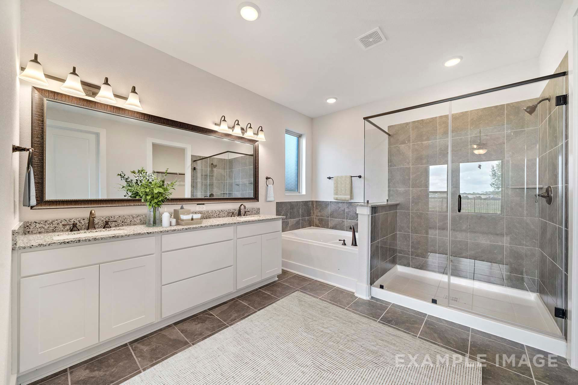 Master bathroom in The Victoria featuring double vanity, garden tub, and glass walk-in shower in main floor primary suite