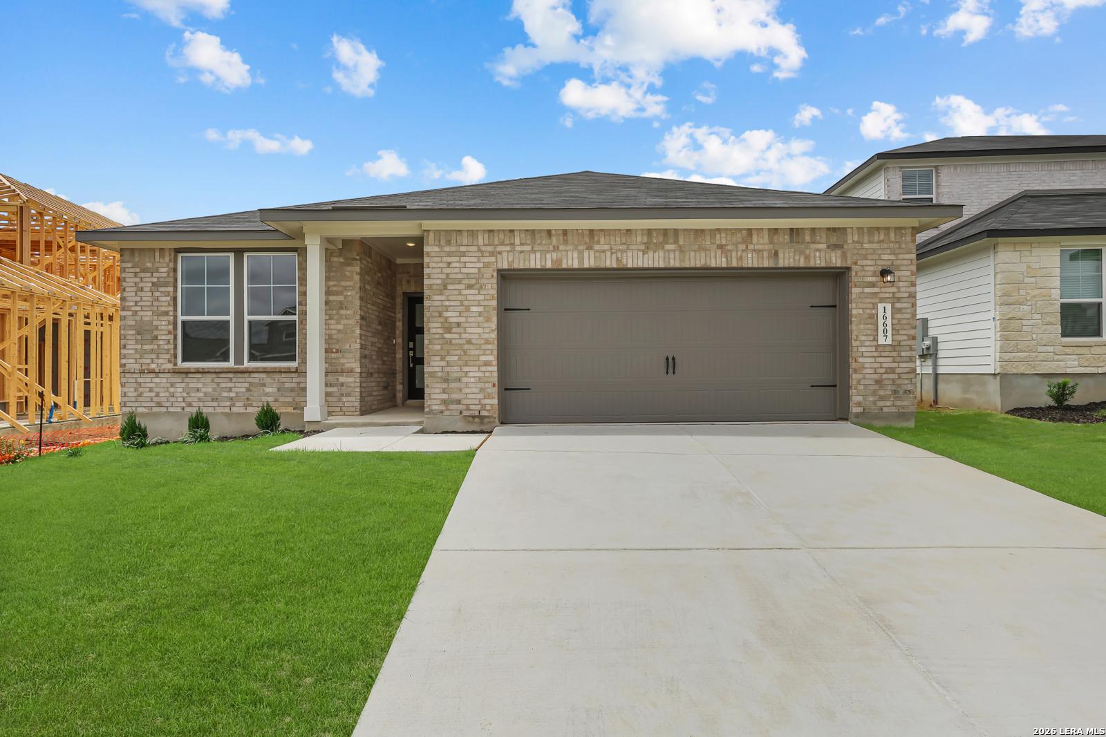 Modern single-story brick home with 2-car garage, covered porch, and green lawn in Hickory Ridge, Elmendorf, Texas