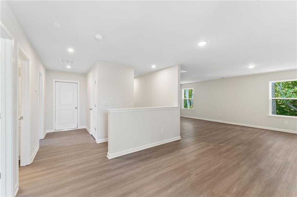 Bright hallway with white doors, open railing, hardwood floors, and window view in 3-bedroom Davidson Homes The Ash B, Riverwood, Dallas, GA