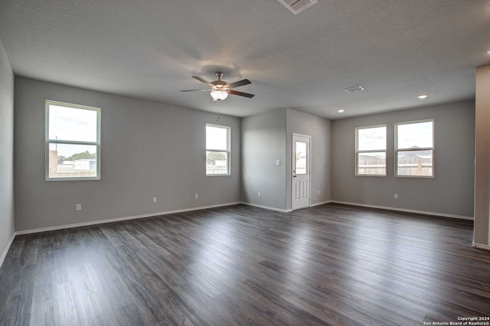 Spacious living room with gray walls, ceiling fan, large windows, and wood flooring in The Daphne J by Davidson Homes, Seguin, Texas