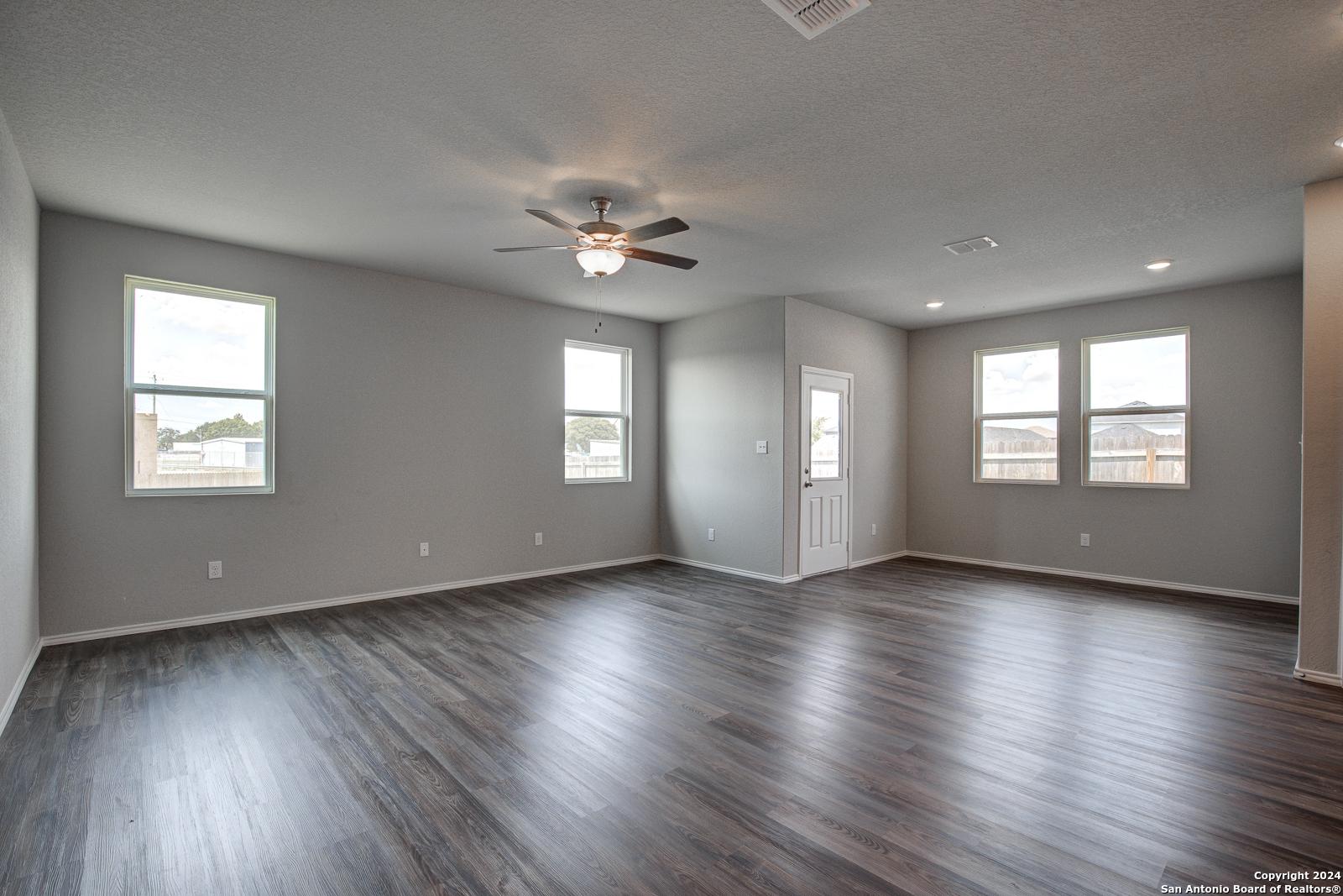 Spacious living room with gray walls, ceiling fan, large windows, and wood flooring in The Daphne J by Davidson Homes, Seguin, Texas