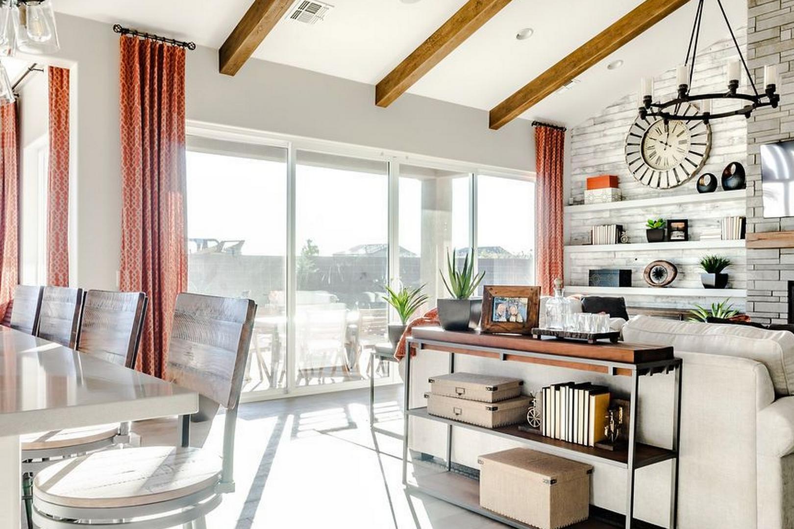 Open-concept living and dining area in The Monarch B with exposed wood beams, stone fireplace, white island, and large sliding doors