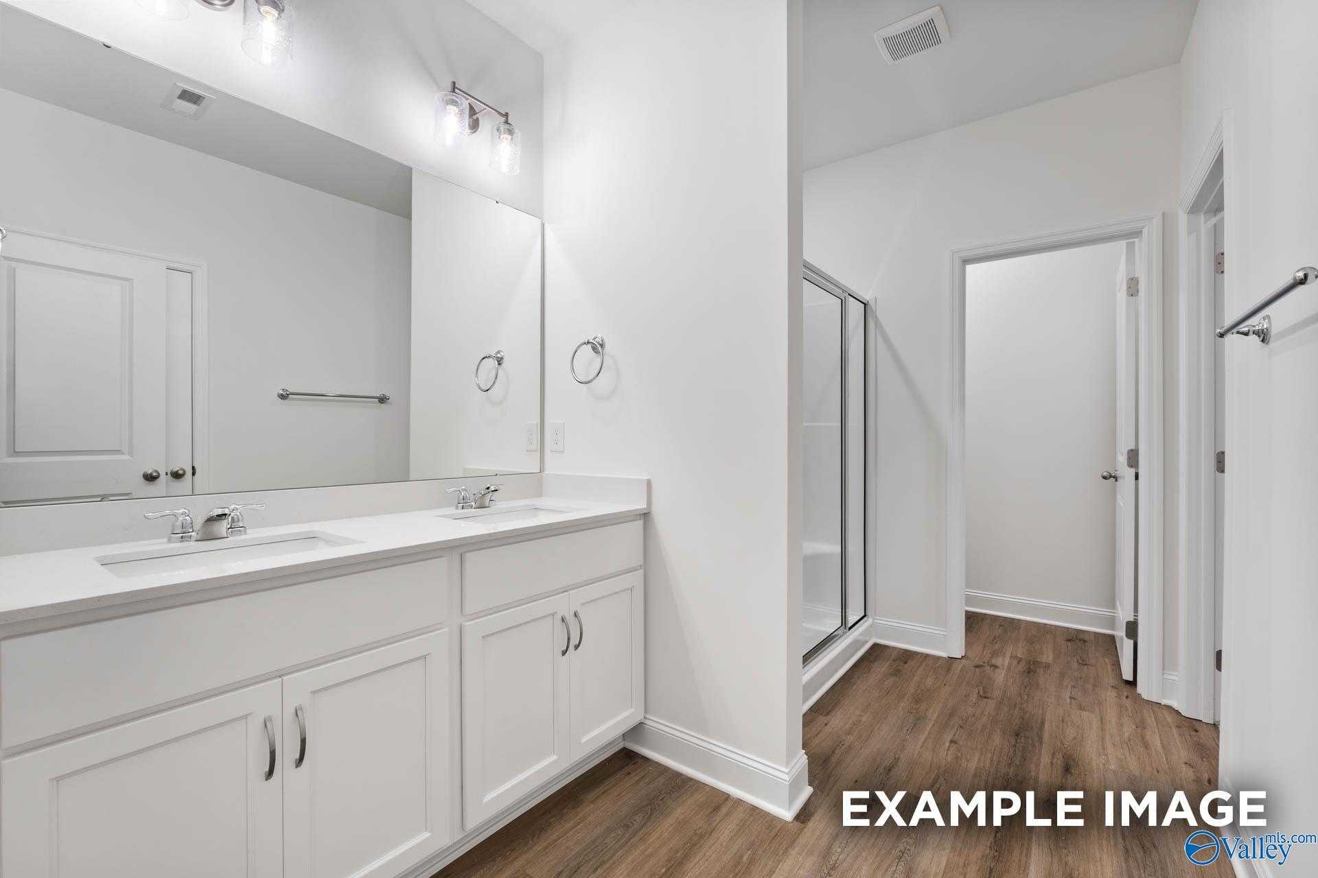 Elegant master bathroom with double white vanity, glass shower, and hardwood floors in The Daphne V by Davidson Homes, Athens, Alabama