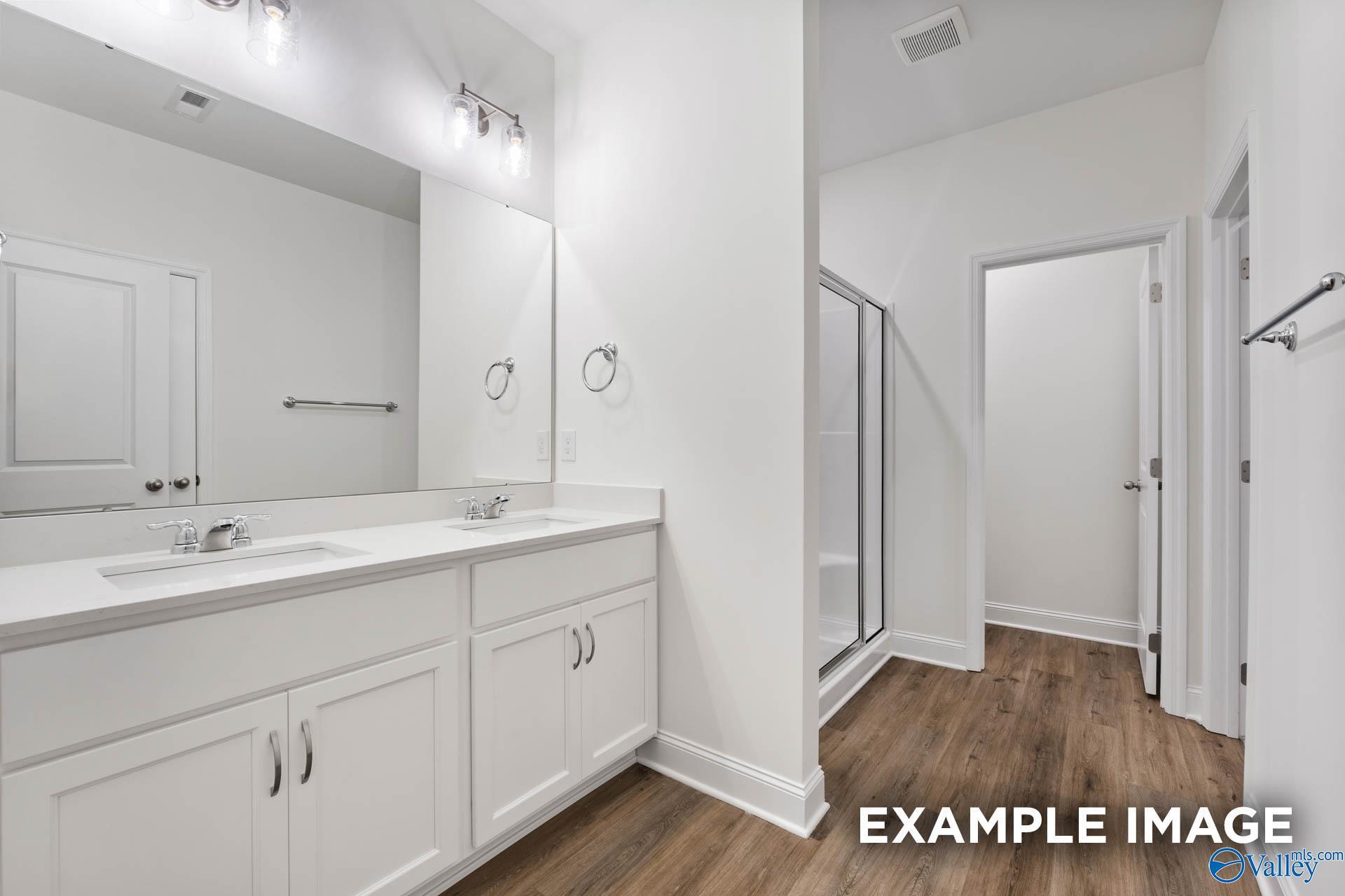 Elegant master bathroom with double white vanity, glass shower, and hardwood floors in The Daphne V by Davidson Homes, Athens, Alabama