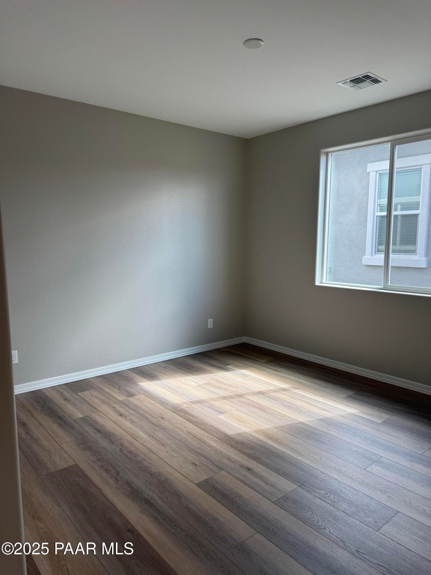 Bright empty bedroom with neutral walls, large window, and luxury vinyl plank floors in Davidson Homes The Monarch A, Prescott AZ