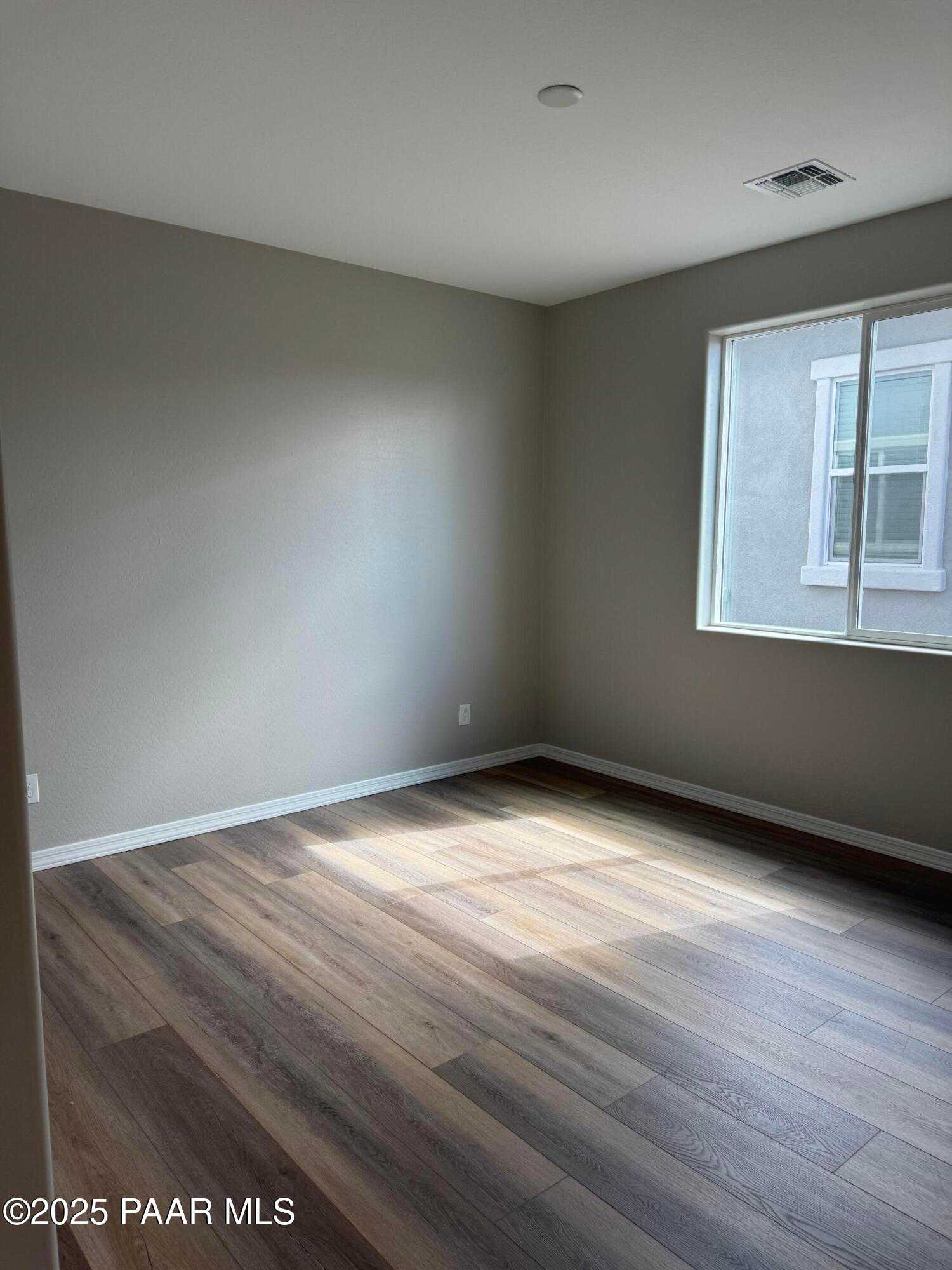 Bright empty bedroom with neutral walls, large window, and luxury vinyl plank floors in Davidson Homes The Monarch A, Prescott AZ