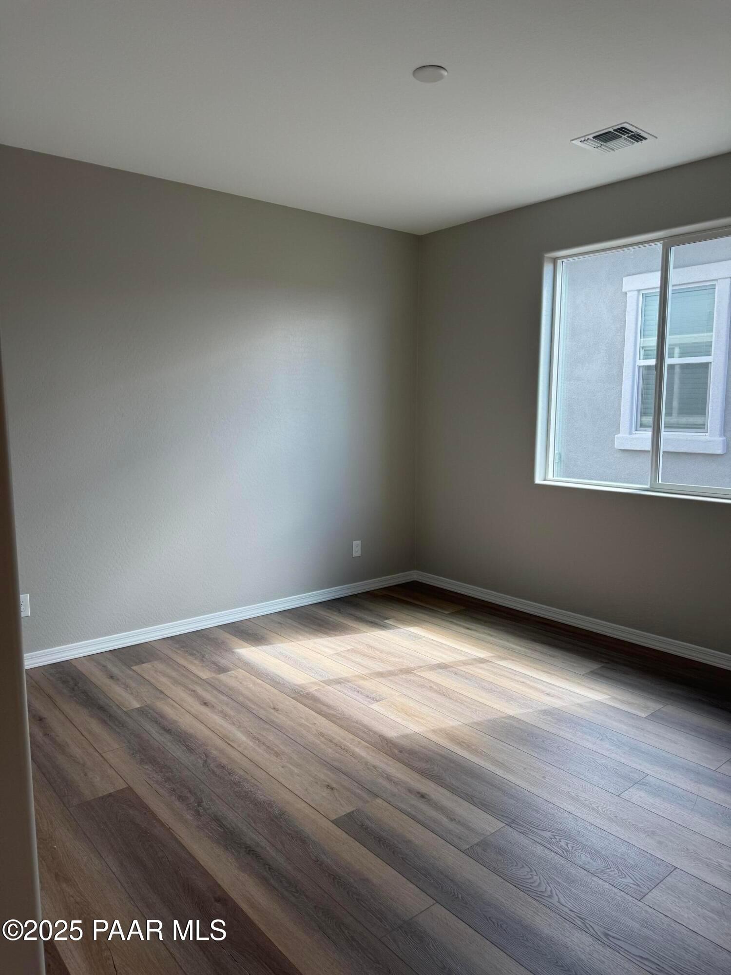 Bright empty bedroom with neutral walls, large window, and luxury vinyl plank floors in Davidson Homes The Monarch A, Prescott AZ