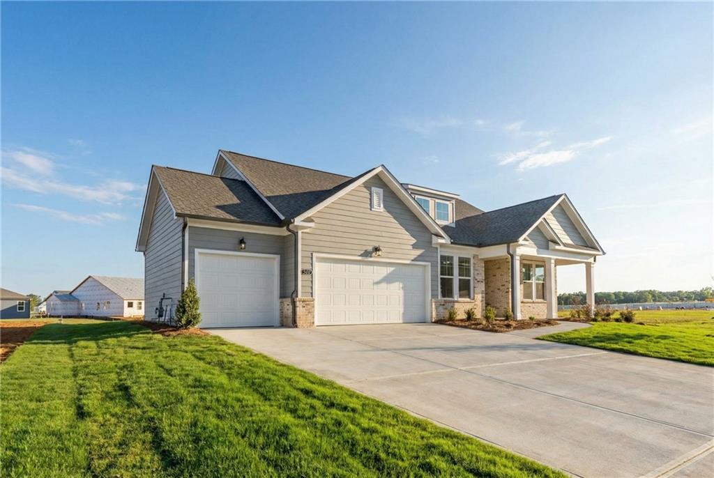 Gray single-story 4-bedroom home with 3-car garage, covered porch, driveway, and lush lawn in Wehunt Meadows, Hoschton, Georgia