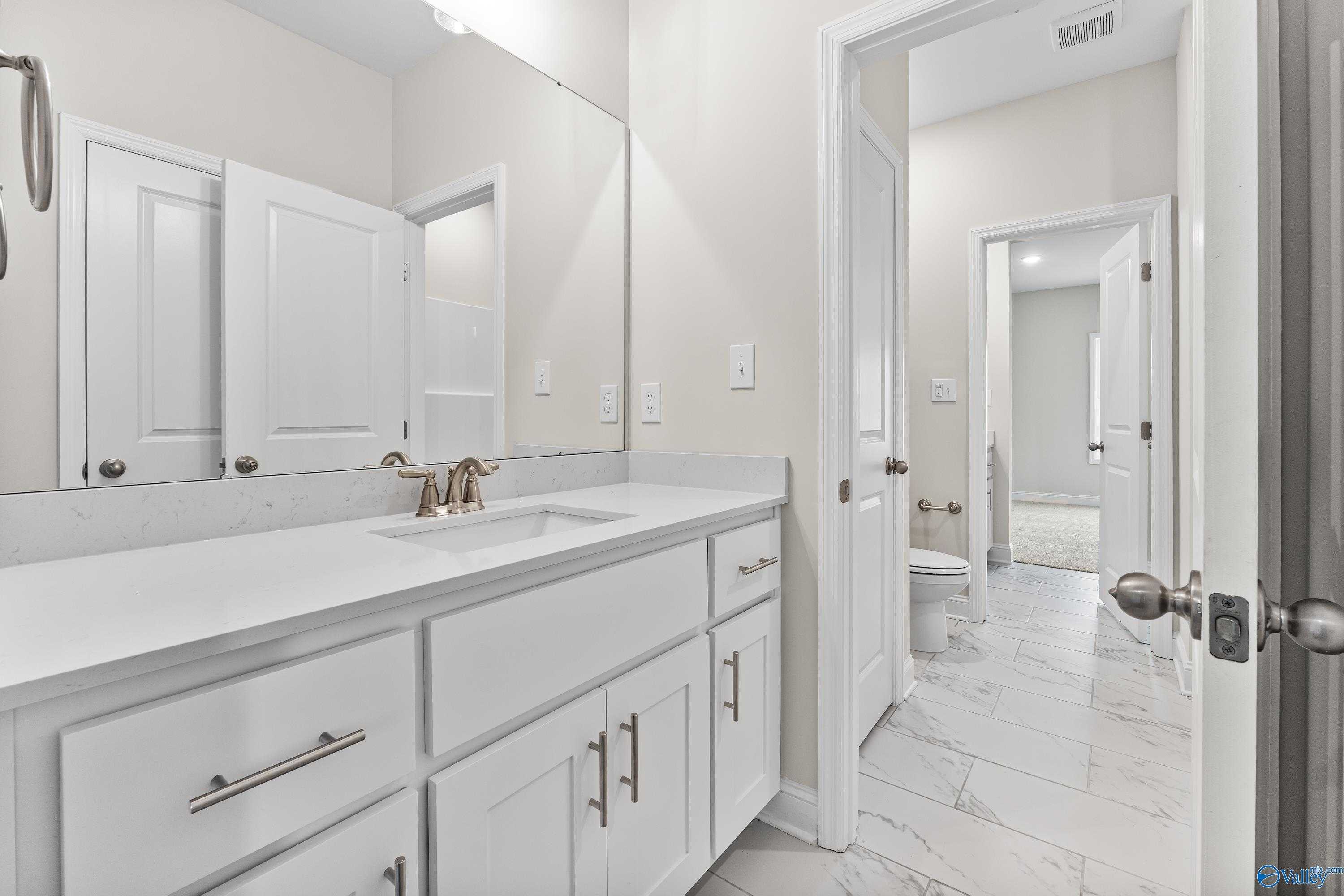 Elegant master bathroom vanity with white cabinets, quartz countertop, bronze faucet, and tiled floor in Davidson Homes The Finleigh, Toney, Alabama