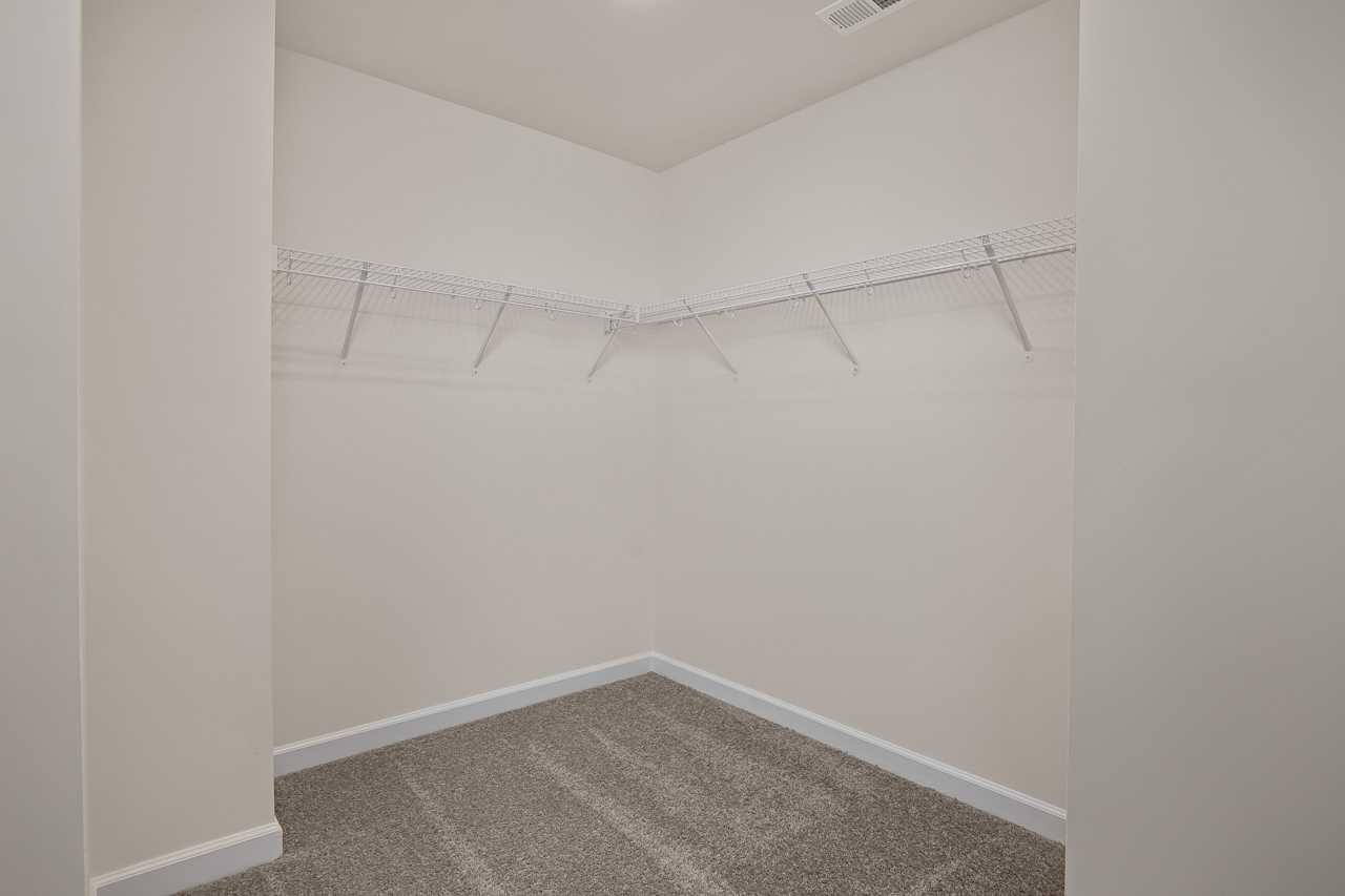 Spacious walk-in closet at Gregory Village Townhomes in Lillington, NC with wire shelving and beige carpet