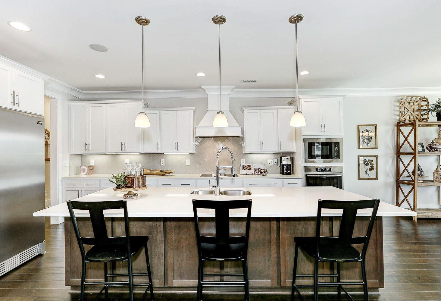 Spacious gourmet kitchen in The Finleigh with white shaker cabinets, large island, black bar stools, and stainless steel appliances