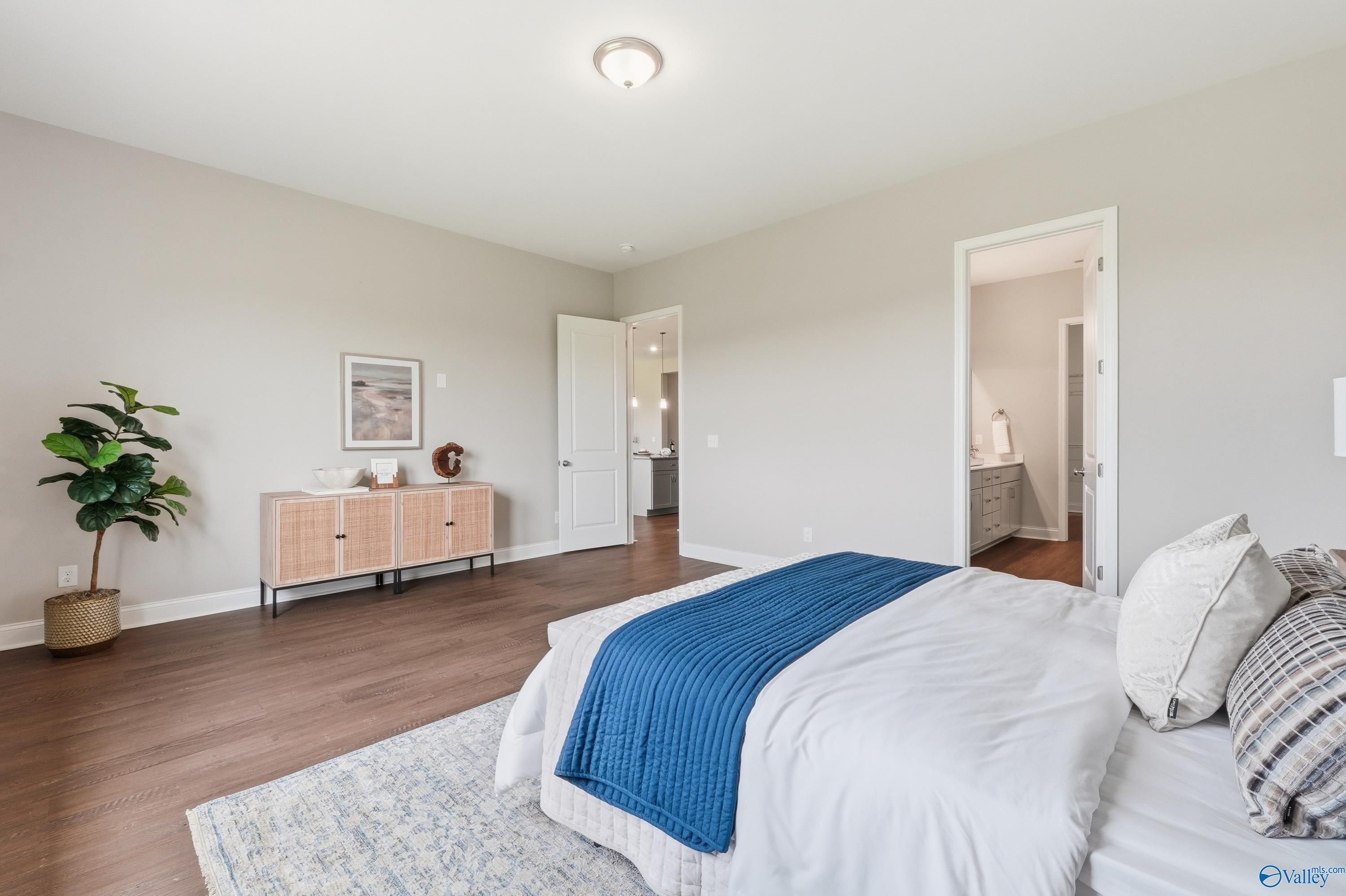Elegant master bedroom with king bed, white duvet, blue throw, hardwood floors, rattan credenza, and en-suite bath in Davidson Homes Arcadia B, Huntsville