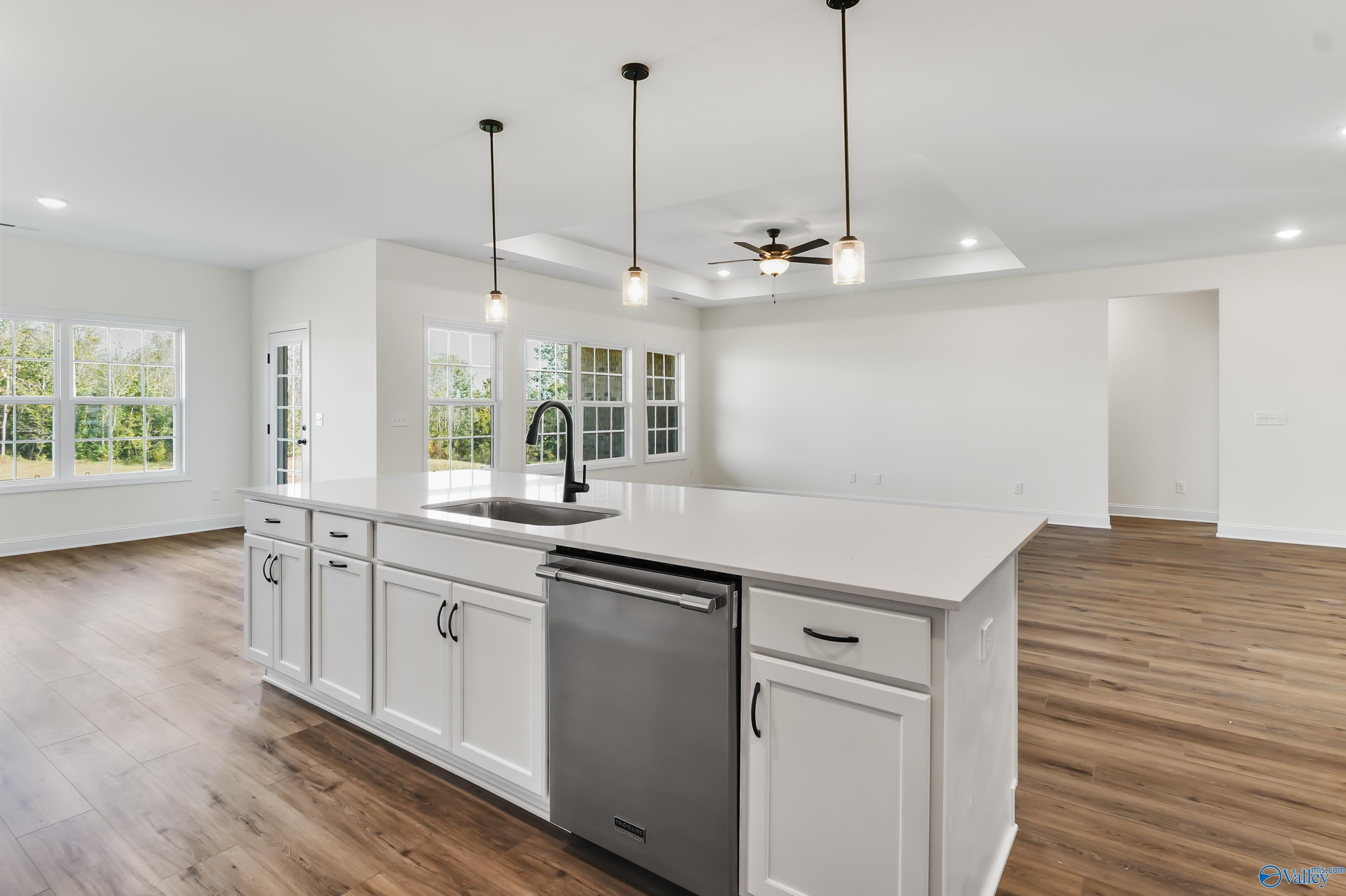 Modern white kitchen with quartz island, farmhouse sink, stainless dishwasher, pendant lights in The Finleigh by Davidson Homes, Harvest AL