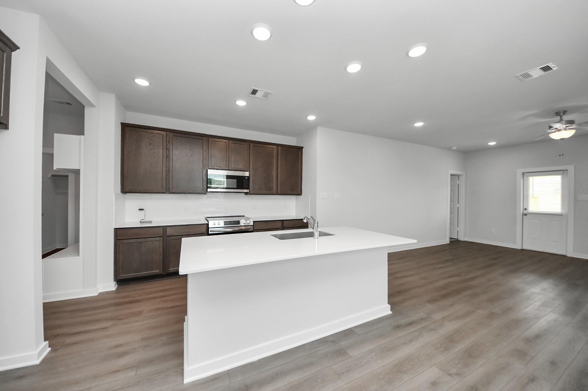 Open-concept kitchen with white quartz island and dark wood cabinets in The Brazos F floor plan, Liberty Estates, Texas.