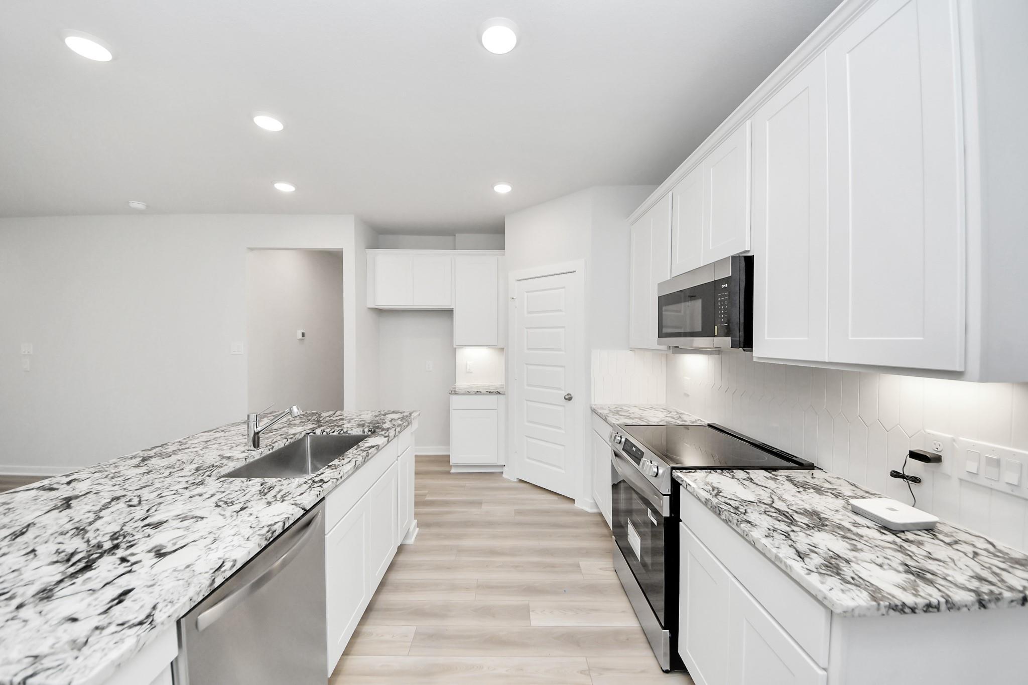 Modern kitchen with white cabinets, granite countertops, and stainless appliances in The Sabine F floor plan, Cleveland, TX.