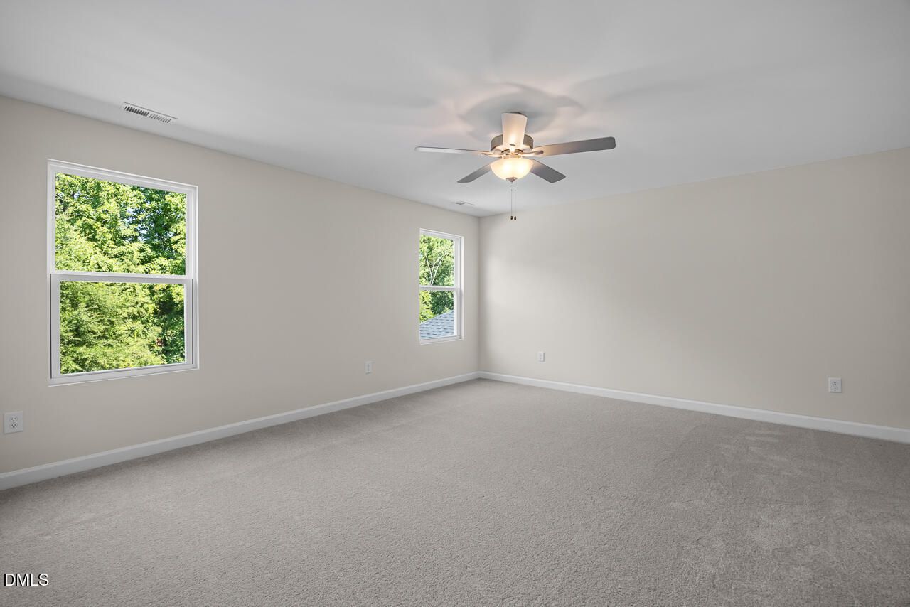 Spacious carpeted bedroom with ceiling fan and tree-lined windows in Davidson Homes The Willow C, Woodland Crossing, Zebulon NC