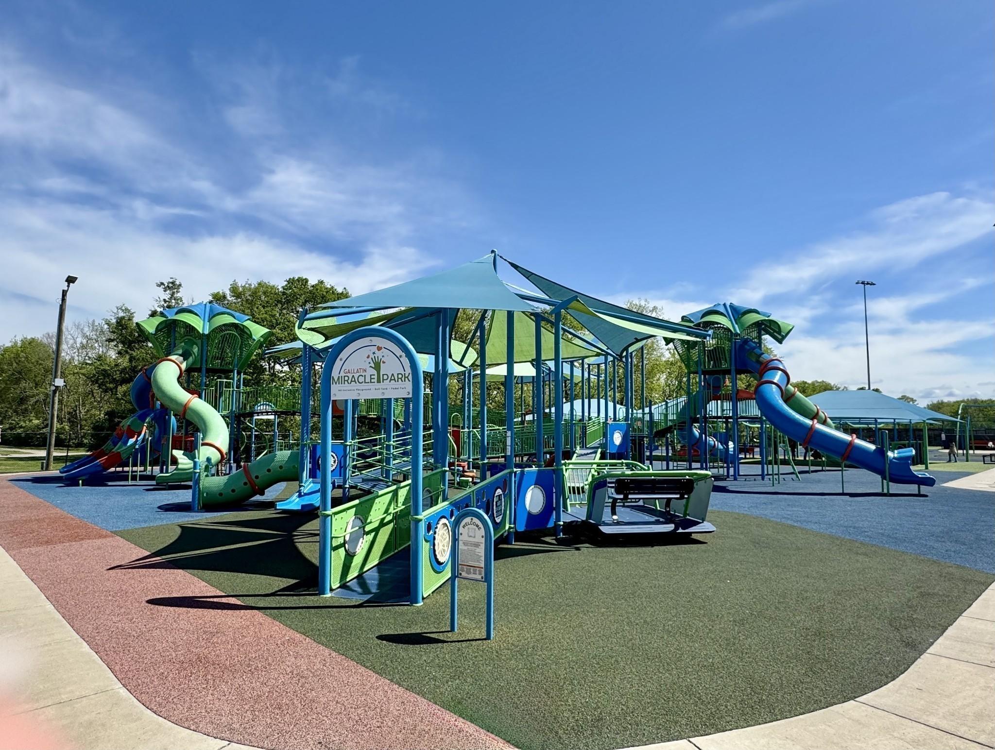 Vibrant playground with green-blue slides, climbing structures, and Woods Crossing sign in Gallatin, Tennessee community