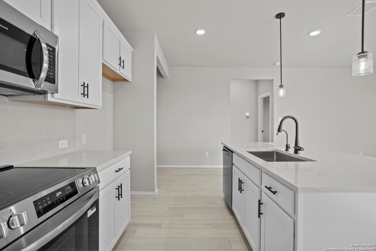 Modern white kitchen with stainless appliances, quartz island sink, and pendant lights in The Daphne H, Davidson Homes, Seguin TX