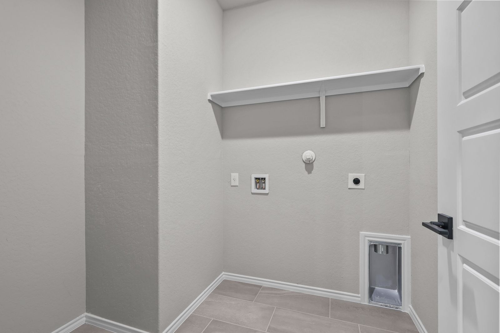 Dedicated laundry room in The Glenwood featuring convenient utility hookups, tile flooring, and overhead storage shelving.
