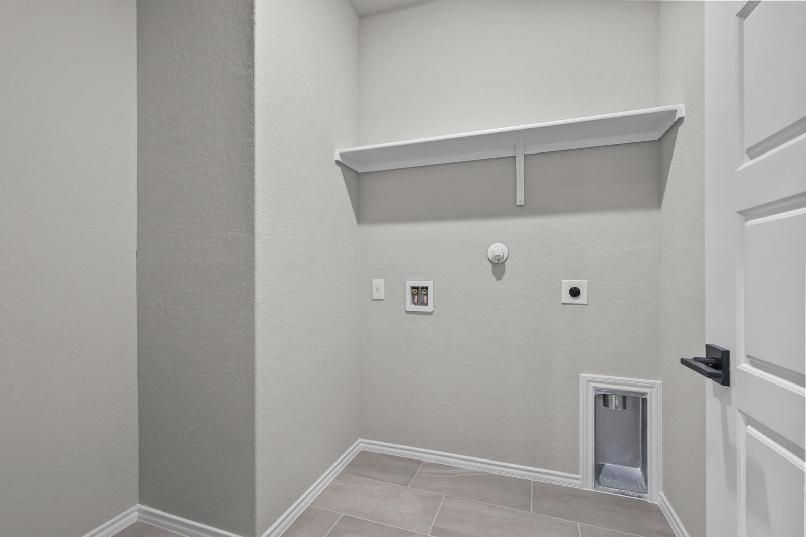 Dedicated laundry room in The Glenwood featuring convenient utility hookups, tile flooring, and overhead storage shelving.