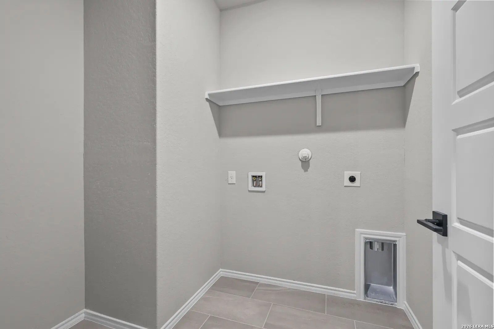Laundry room with washer and dryer hookups and overhead shelving in The Glenwood E home at Comanche Ridge, San Antonio.