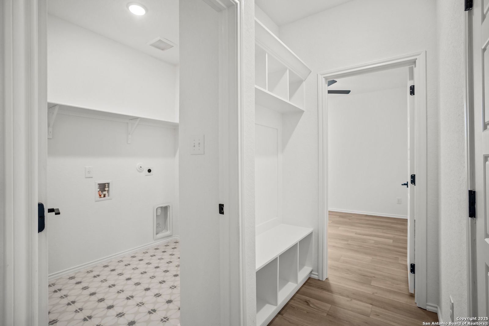 Bright laundry room with washer/dryer hookups, patterned tile floor, and adjacent closet shelving in Davidson Homes The Daphne K, San Antonio